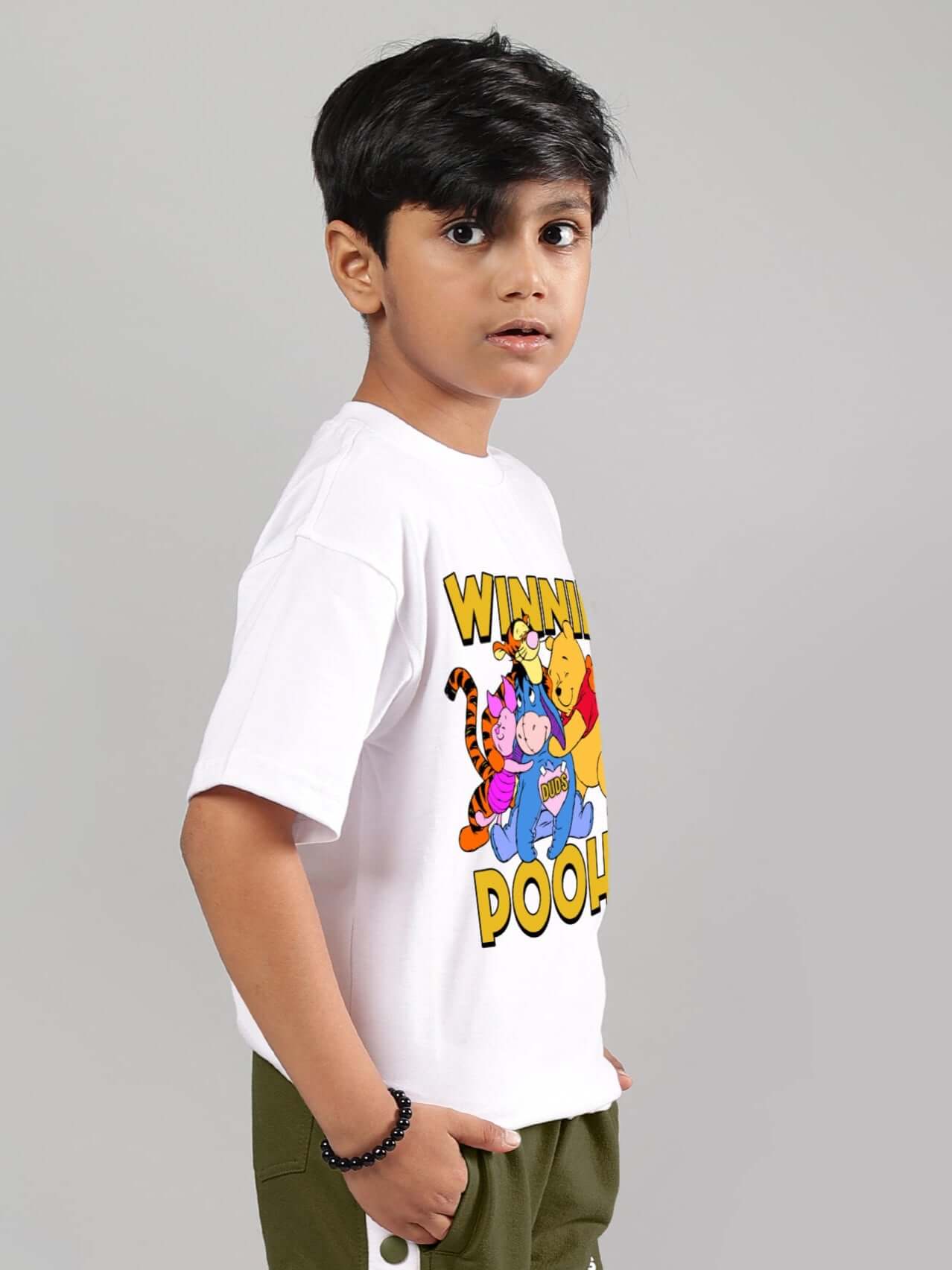 Young boy wearing a white Winnie the Pooh t-shirt featuring colorful characters, ideal for both boys and girls, by DUDS.