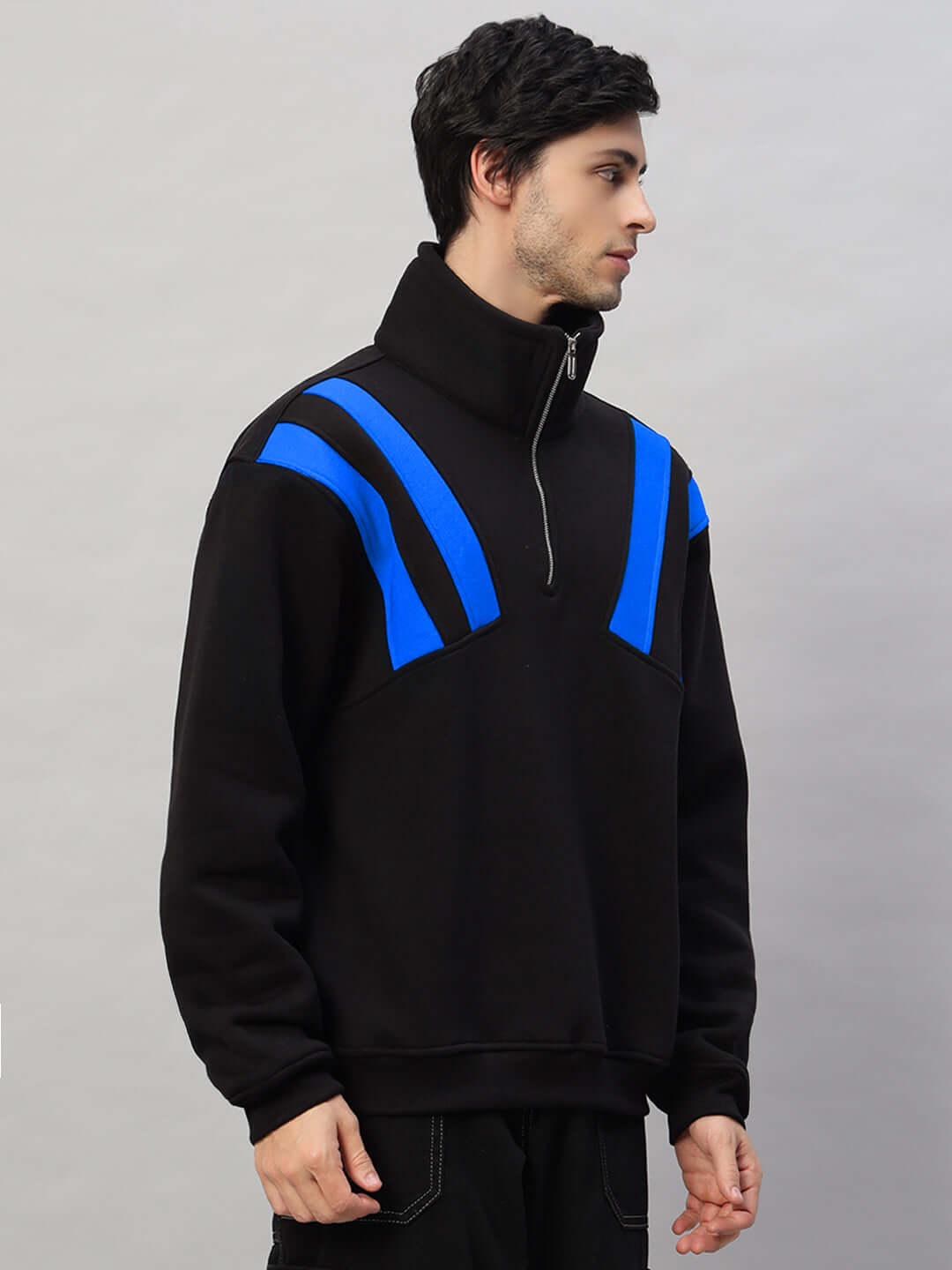 Man wearing a black and blue colorblock crossbar fleece jacket with a high collar and zippered neck, side view.