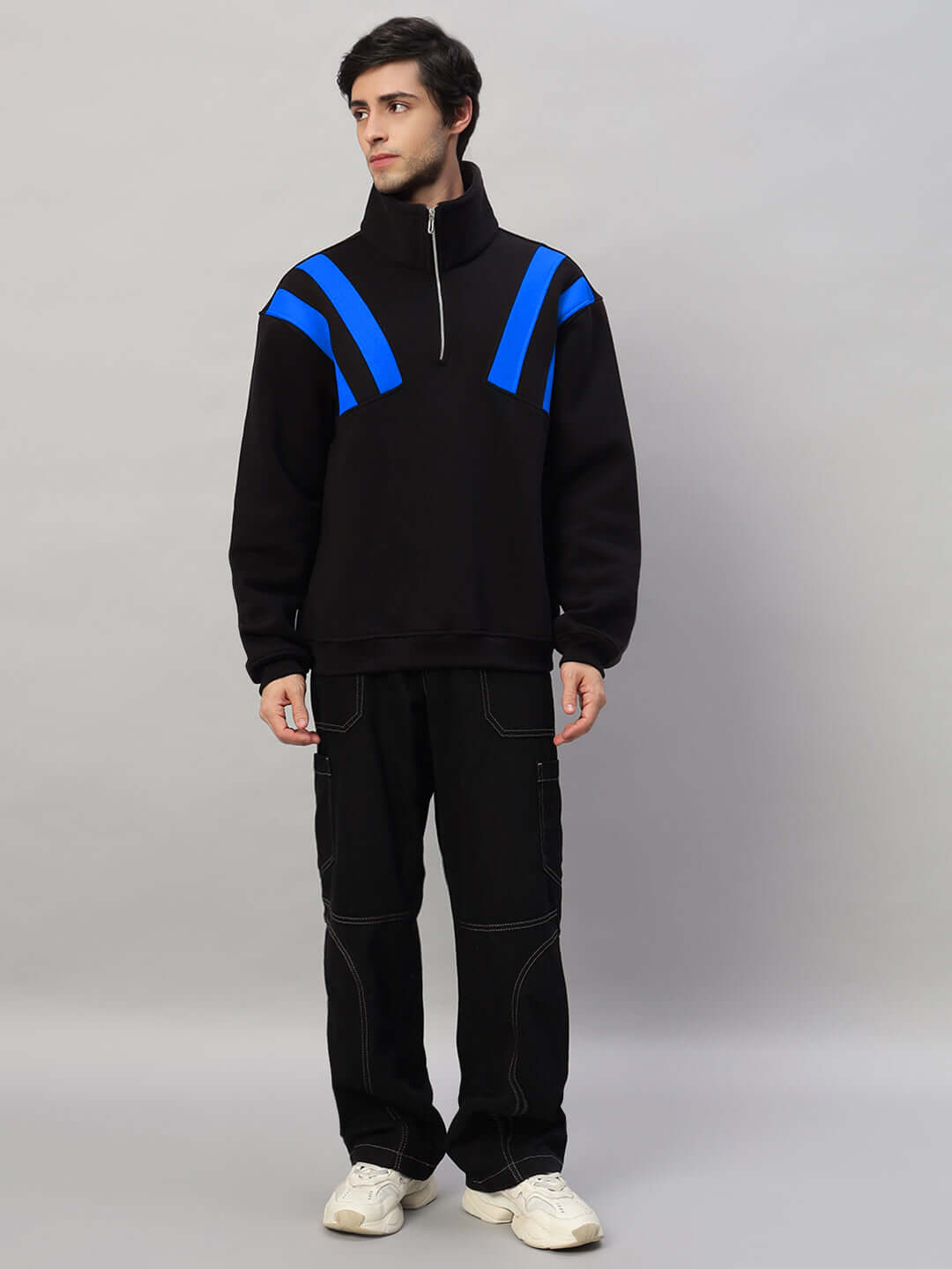 Male model wearing a black fleece jacket with blue colorblock design, paired with black pants and white sneakers.