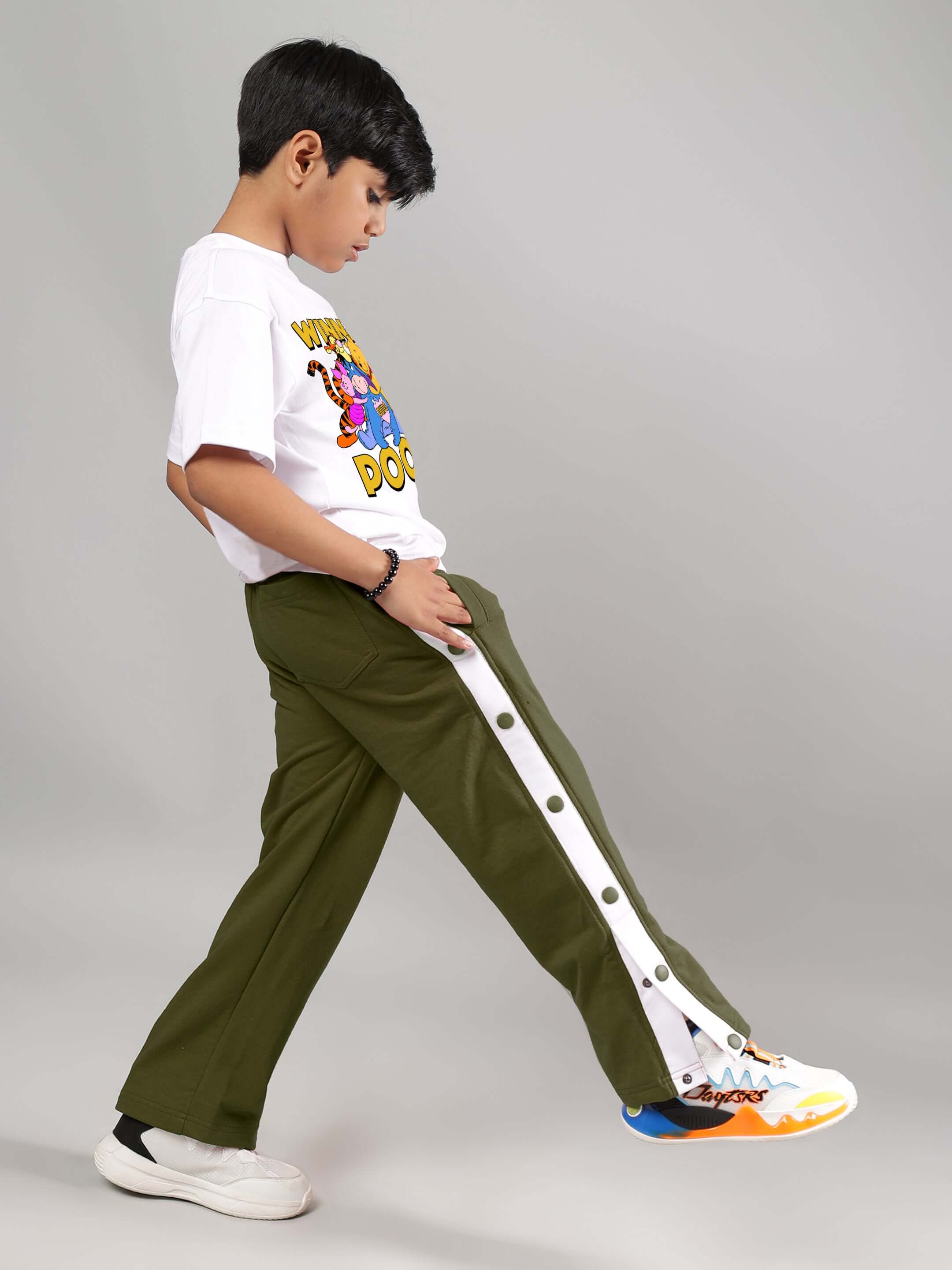 Child wearing white Winnie the Pooh T-shirt and green pants, showcasing playful style for boys and girls.