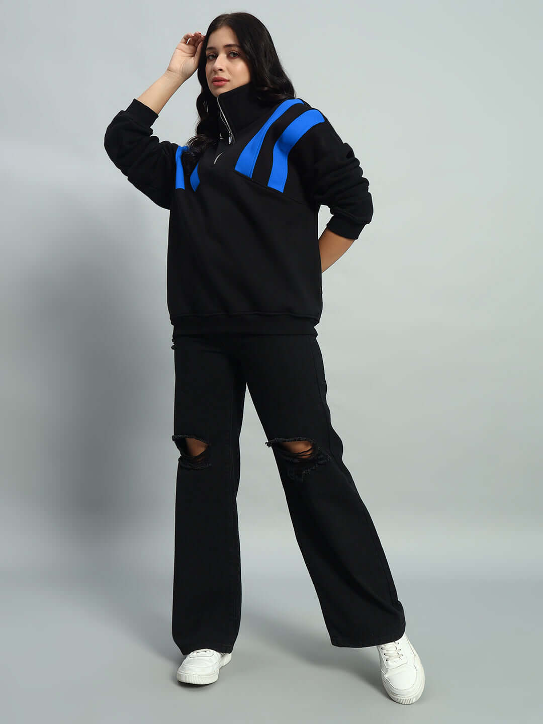 Woman wearing a black and blue colorblock jacket, styled with black ripped jeans and white sneakers, showcasing a modern athletic look.