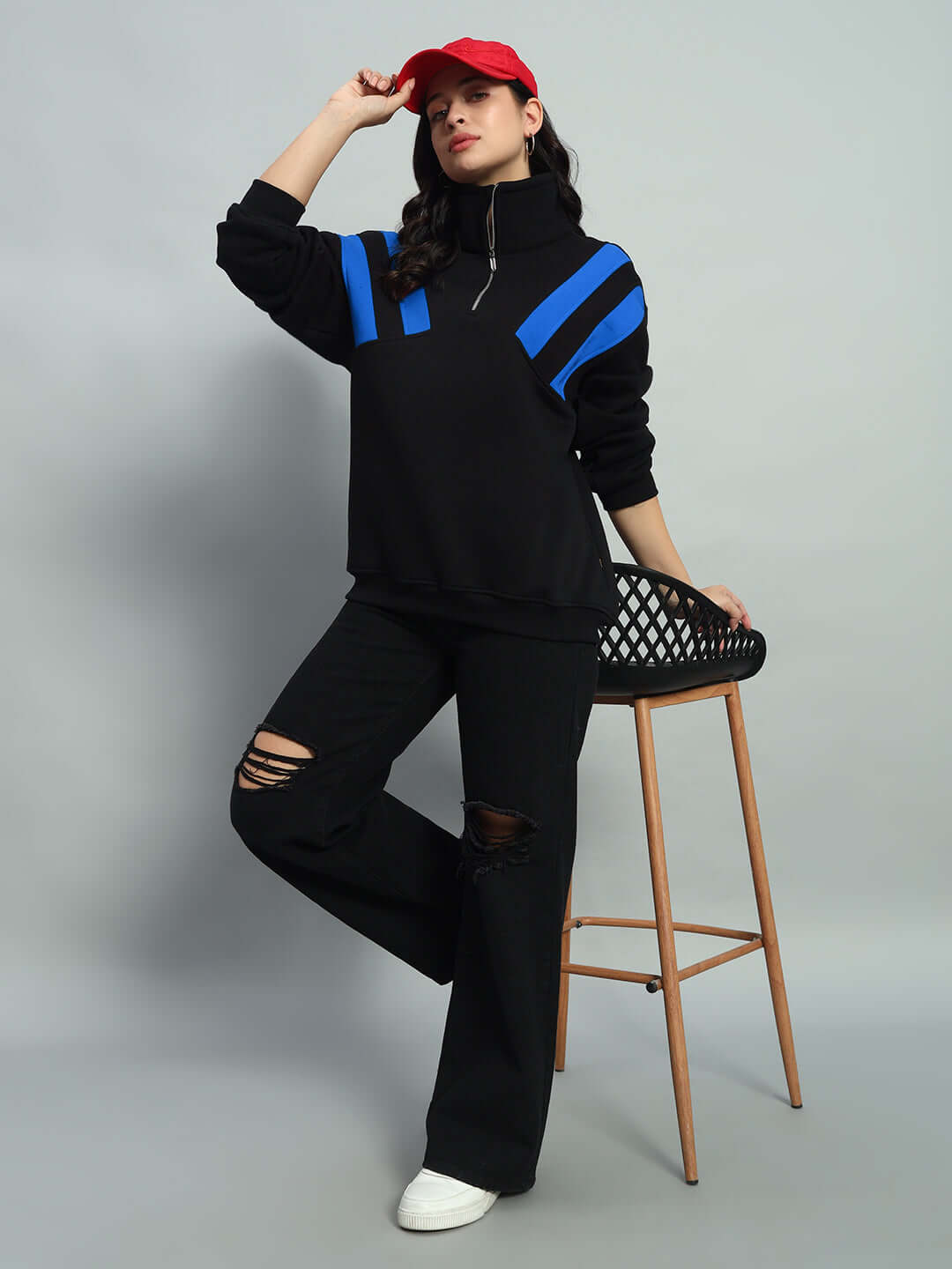 Women's crossbar fleece colorblock jacket in black and royal blue, styled with ripped jeans, red cap, and white sneakers for a sporty chic look.
