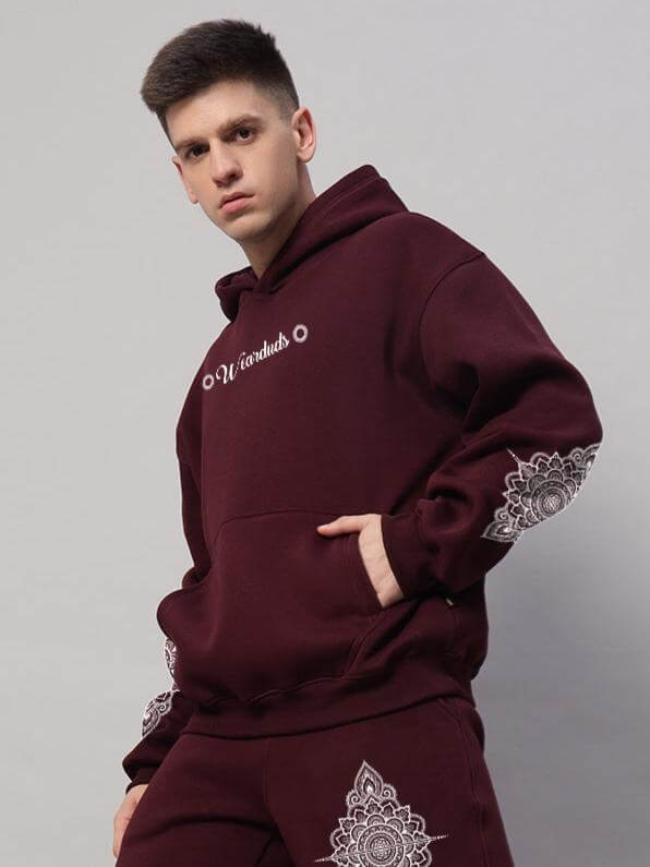 Man wearing Yantra Fleece Hoodie in wine color, featuring mandala designs on sleeves, captures modern streetwear style and comfort.