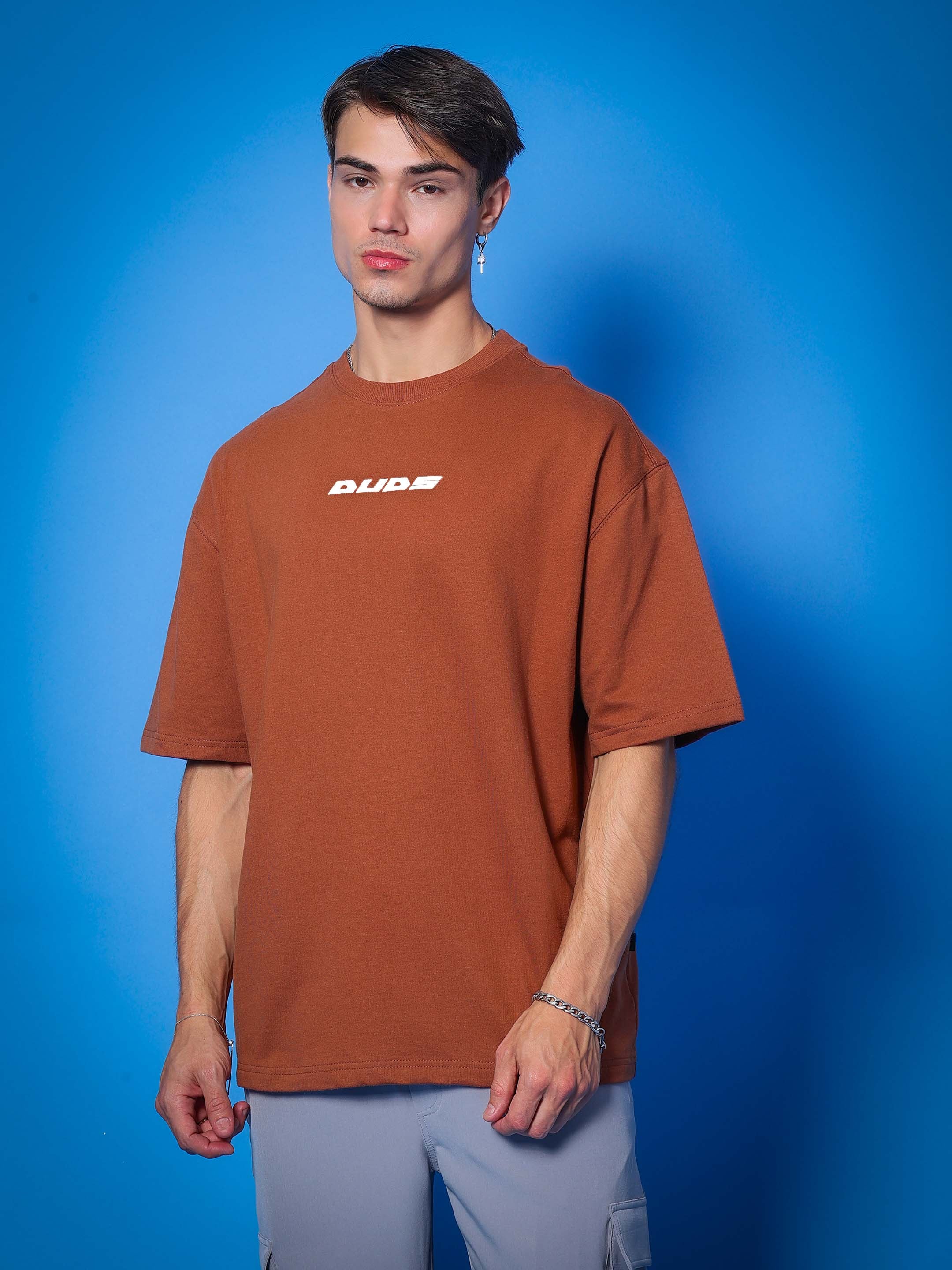 Man wearing a brown PRAY OVER-SIZED COTTON T-SHIRT with premium fabric blend, featuring a relaxed fit.