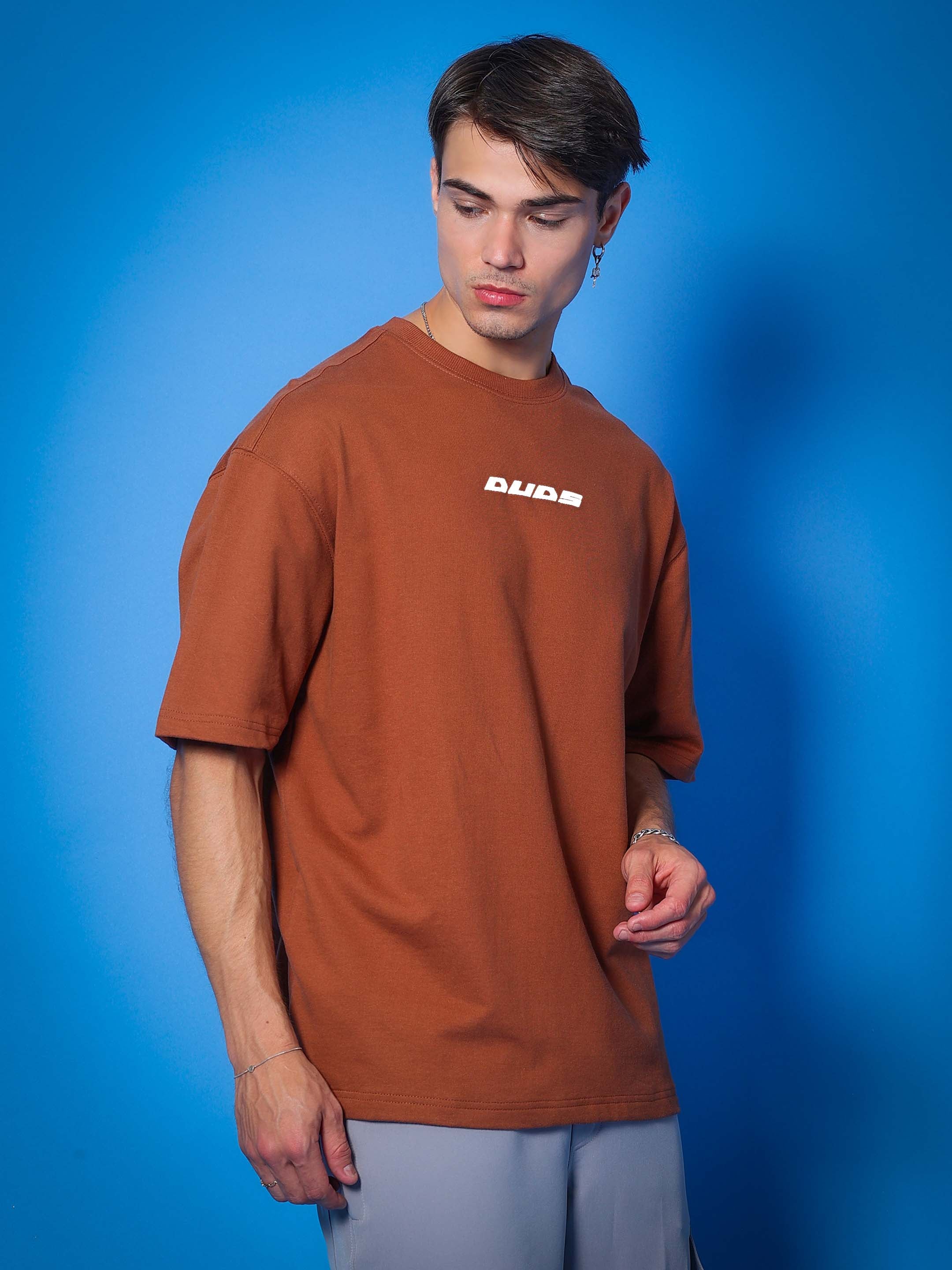 Model wearing PRAY OVER-SIZED COTTON T-SHIRT BROWN with premium fabric, standing against blue background