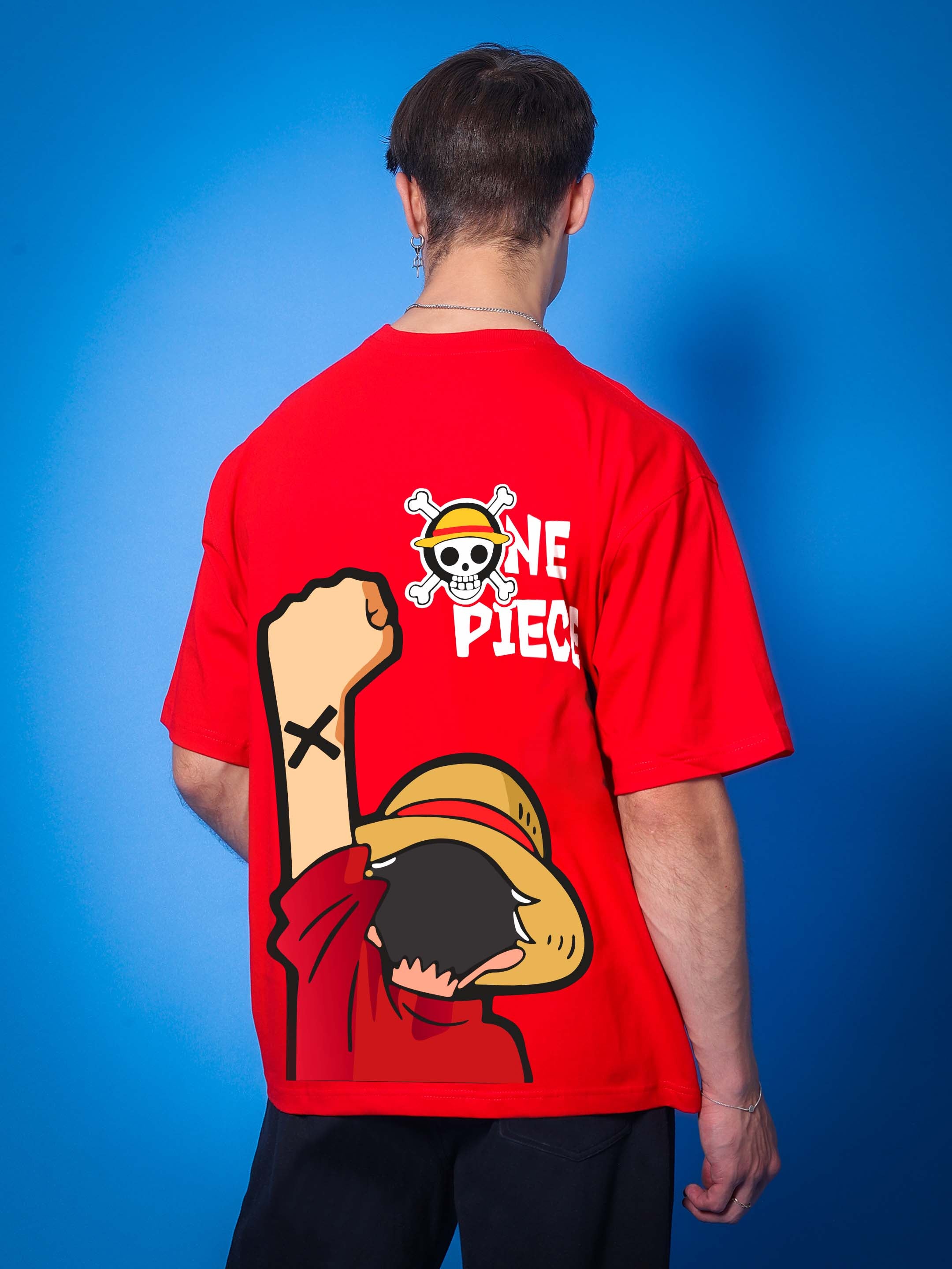 Man wearing ONE PIECE OVER-SIZED T-SHIRT RED with character design on the back, standing against blue background.