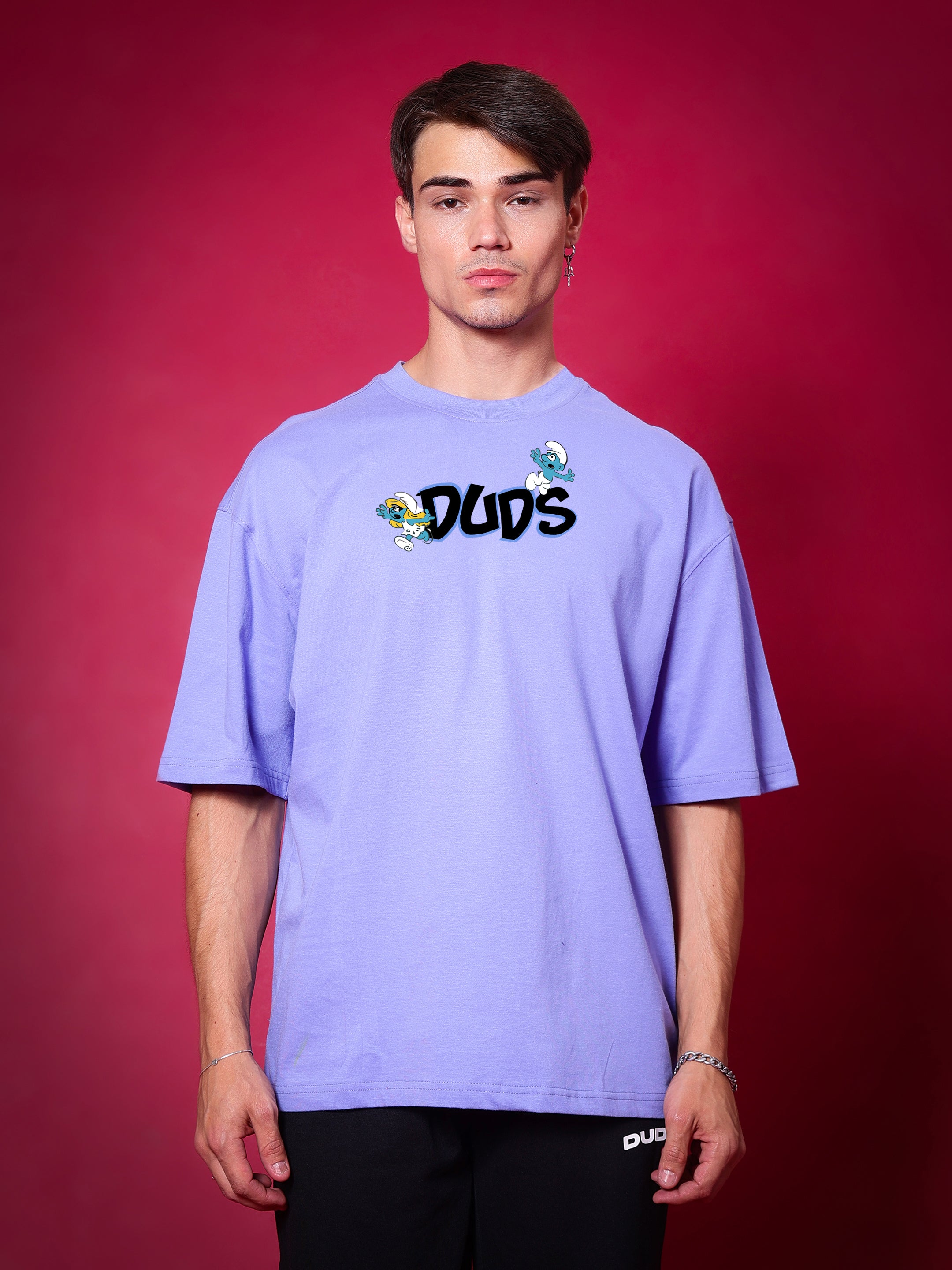 Person wearing SMURFS OVER-SIZED T-SHIRT PURPLE from DUDS collection, showcasing front design on a red background.