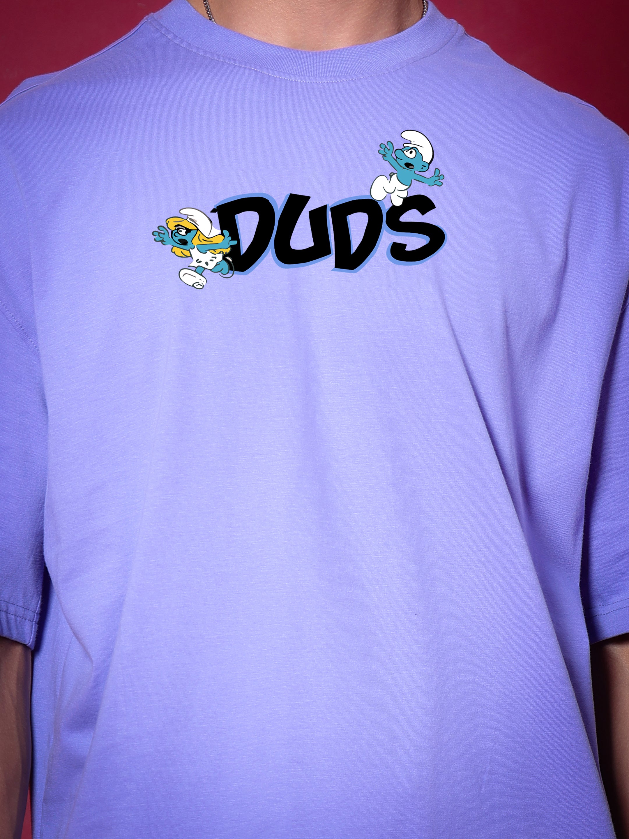 Person wearing SMURFS OVER-SIZED T-SHIRT PURPLE by DUDS with custom fit option available, featuring Smurfs logo on front.