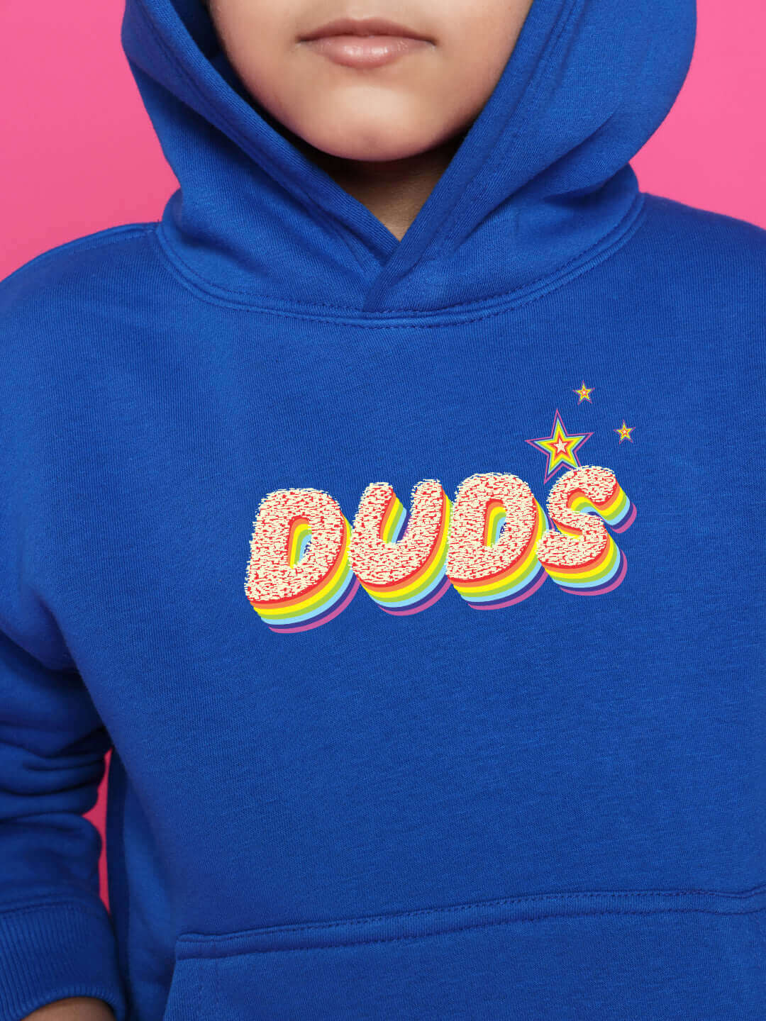 Child in blue hoodie with colorful 'DUDS' logo, pink background.