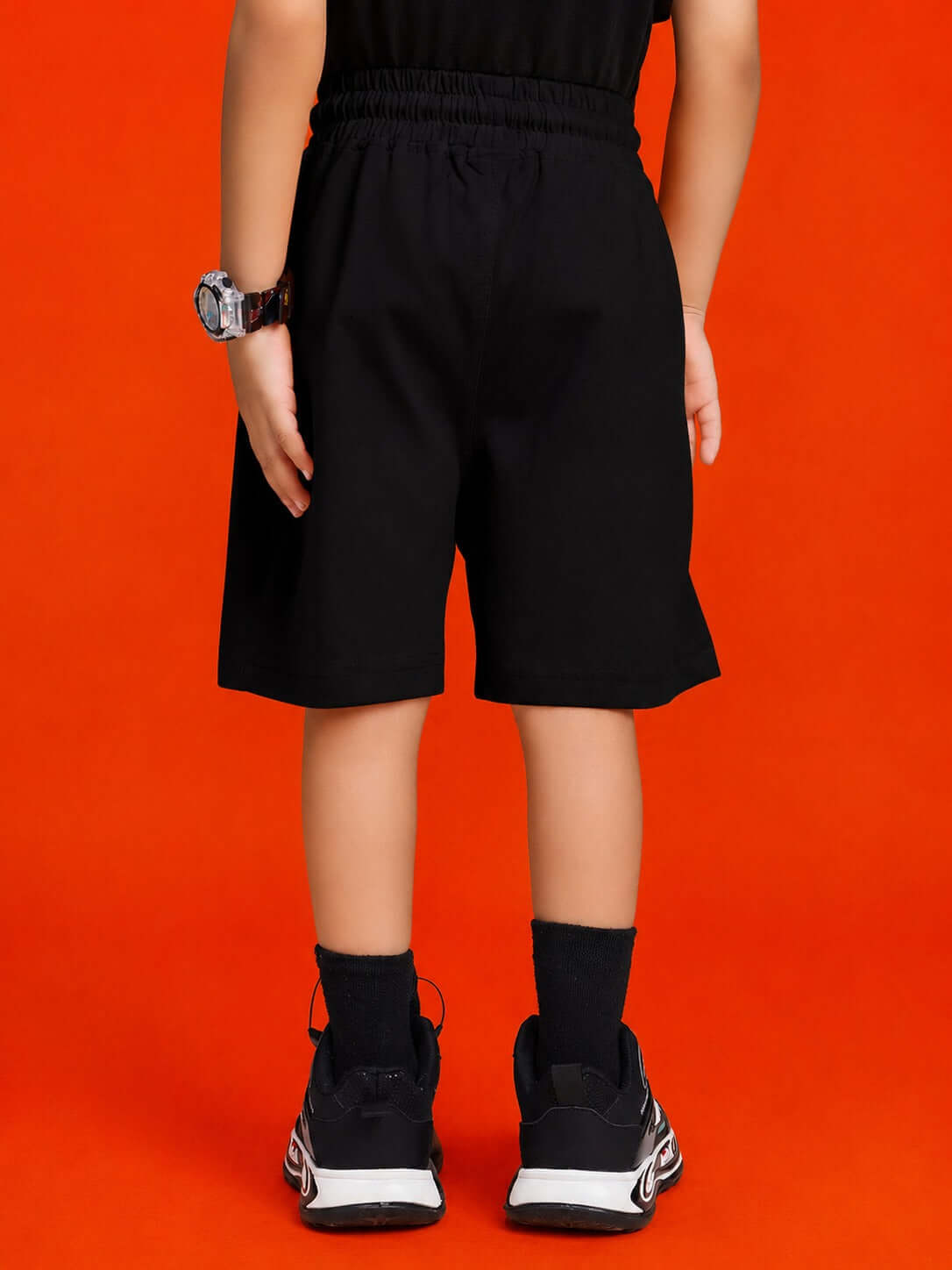 Back view of a kid wearing QUACK ATTACK GRAPHIC CO-ORD SET FOR BOYS GIRLS BLACK with black shorts and sporty shoes.