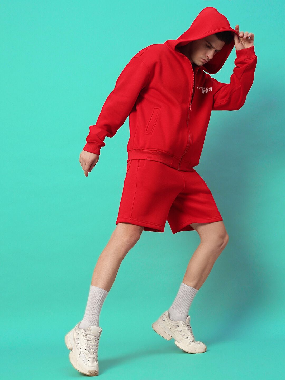 Model wearing A LOOK ATTITUDE FLEECE CO-ORD RED, featuring a stylish and cozy red hoodie and shorts set against a turquoise background.