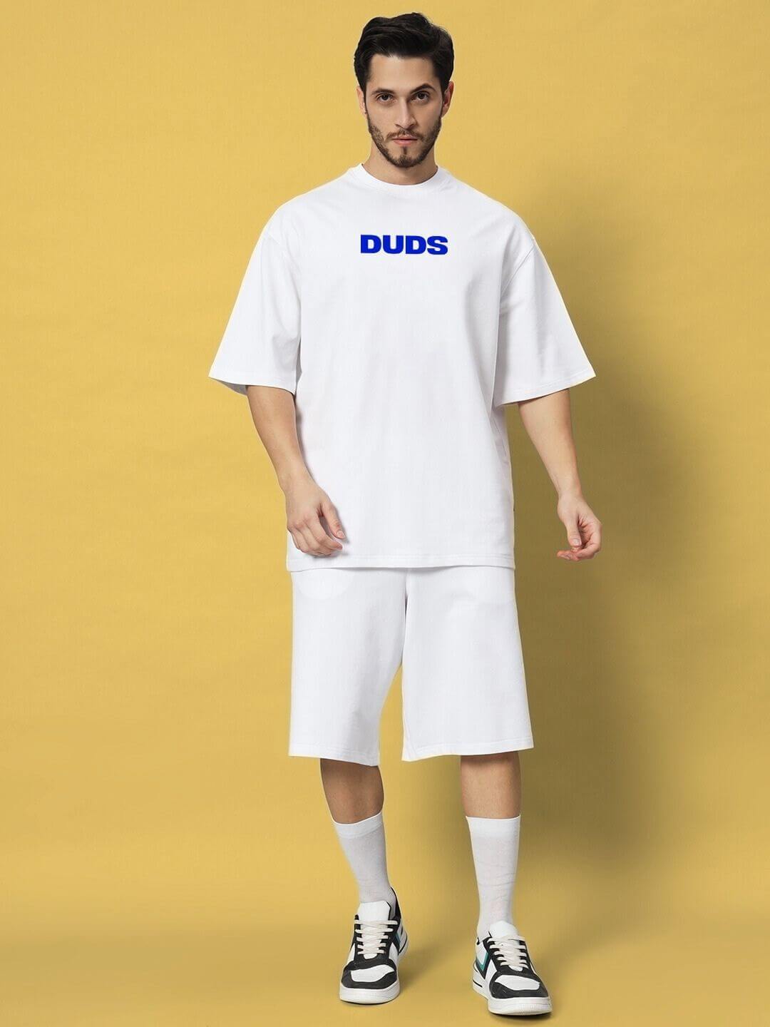 Man wearing ABSENT PRESENT CO-ORD SET WHITE standing against a yellow background, embodying modern minimalism with casual elegance.