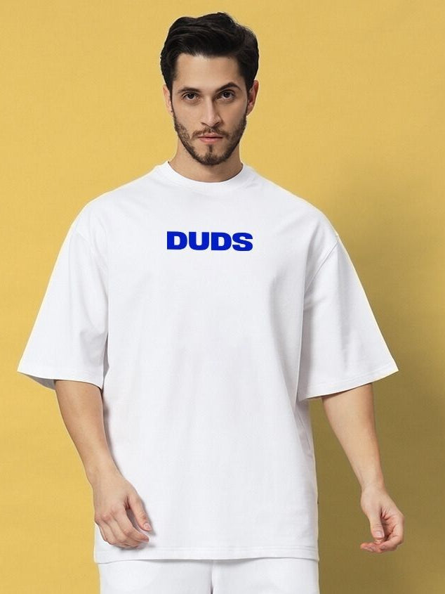 Model wearing ABSENT PRESENT OVER-SIZED T-SHIRT WHITE with blue "DUDS" text on a yellow background.
