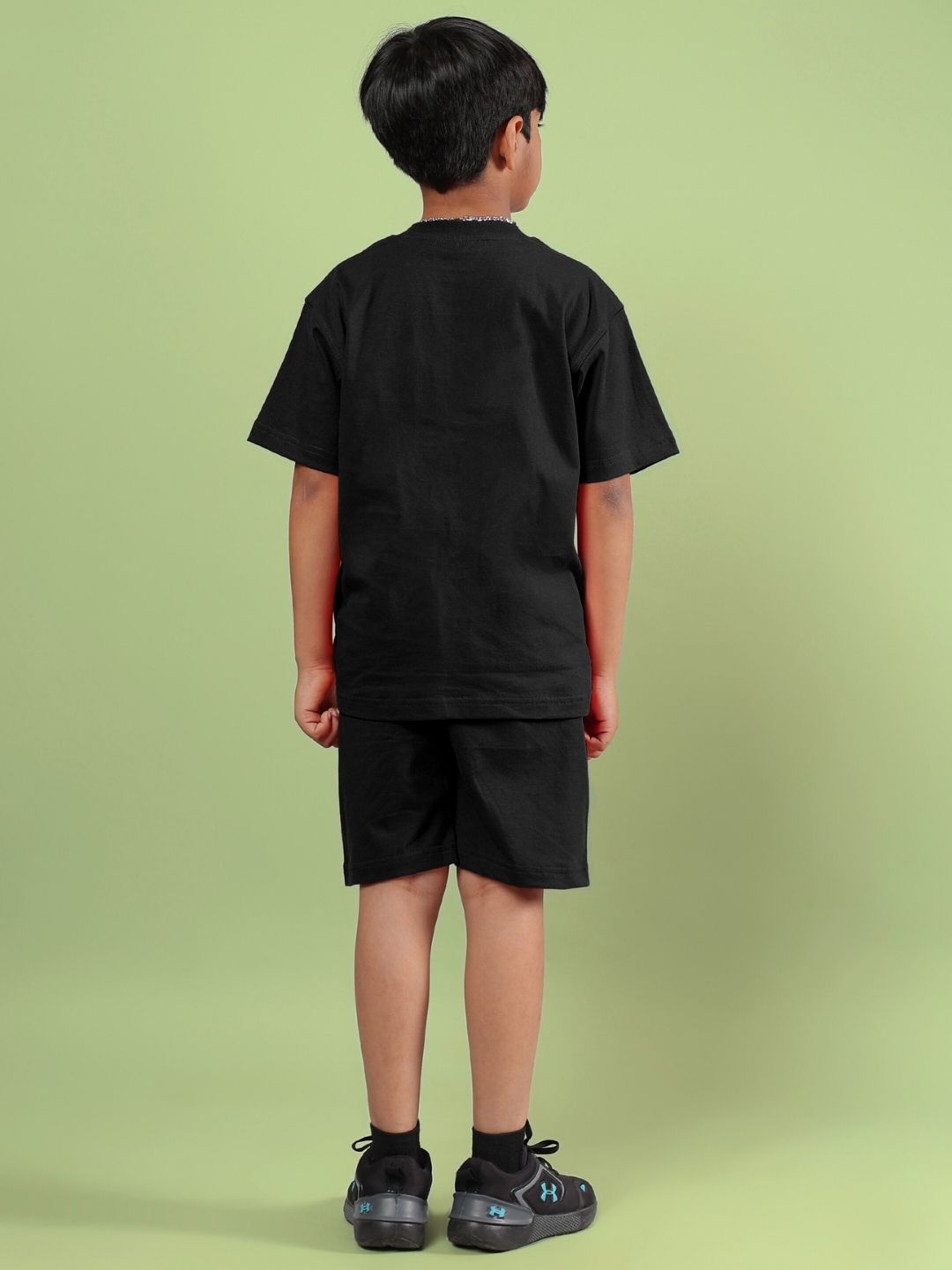 Child wearing ACE co-ord set for boys and girls in black, viewed from behind, standing on a green background.