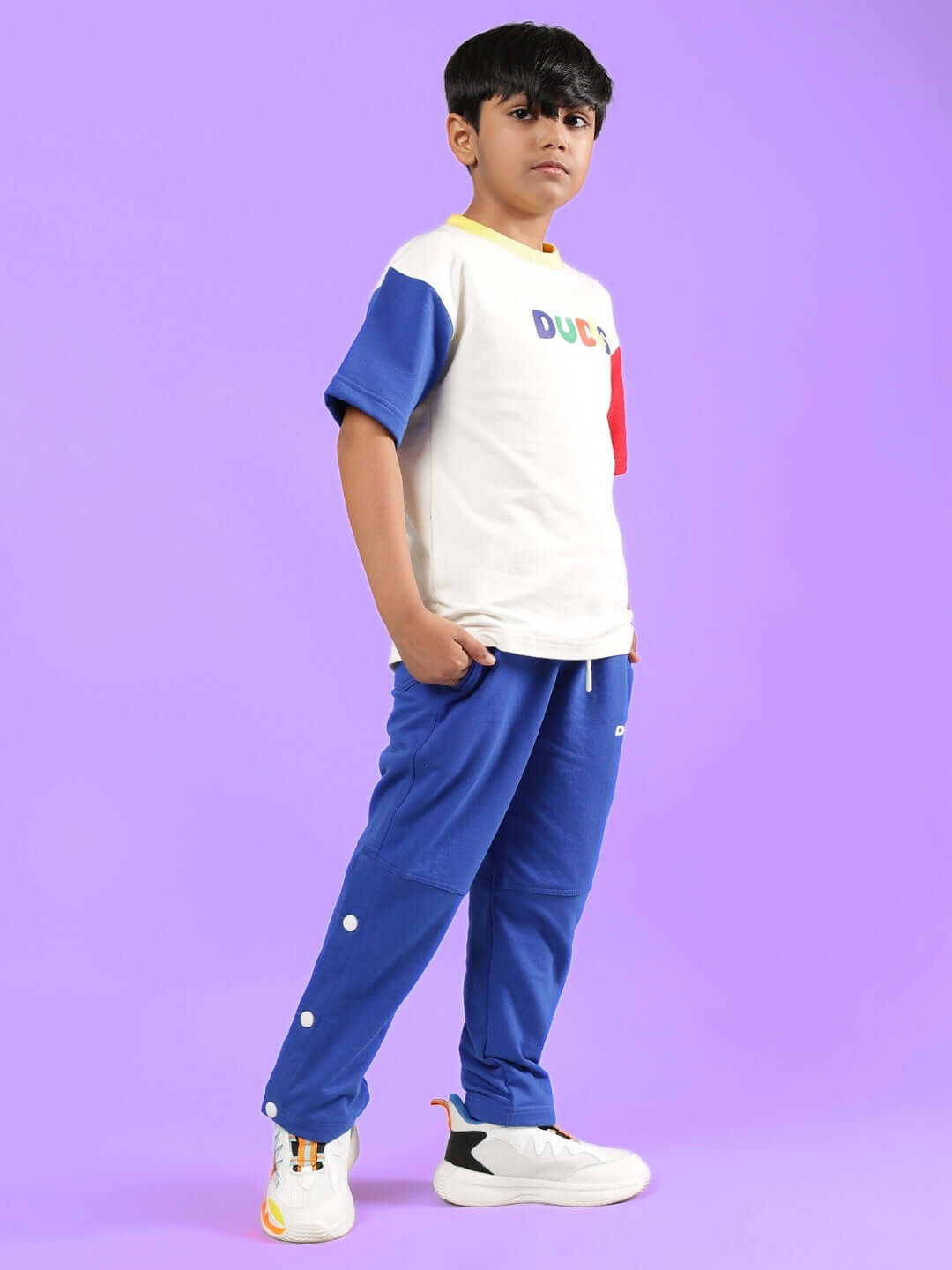 Boy wearing ADONIS co-ord set in off white and royal blue against a purple background