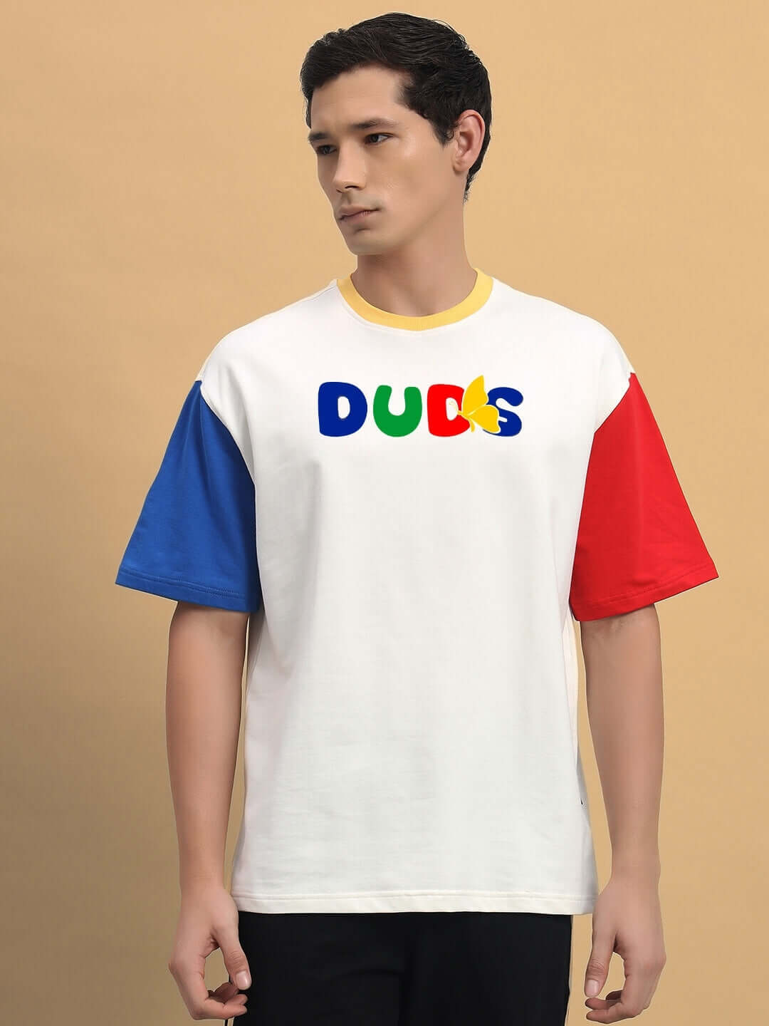 Man wearing ADONIS Color Blocked Oversized T-Shirt in off-white with blue and red sleeves, bold text design on front.
