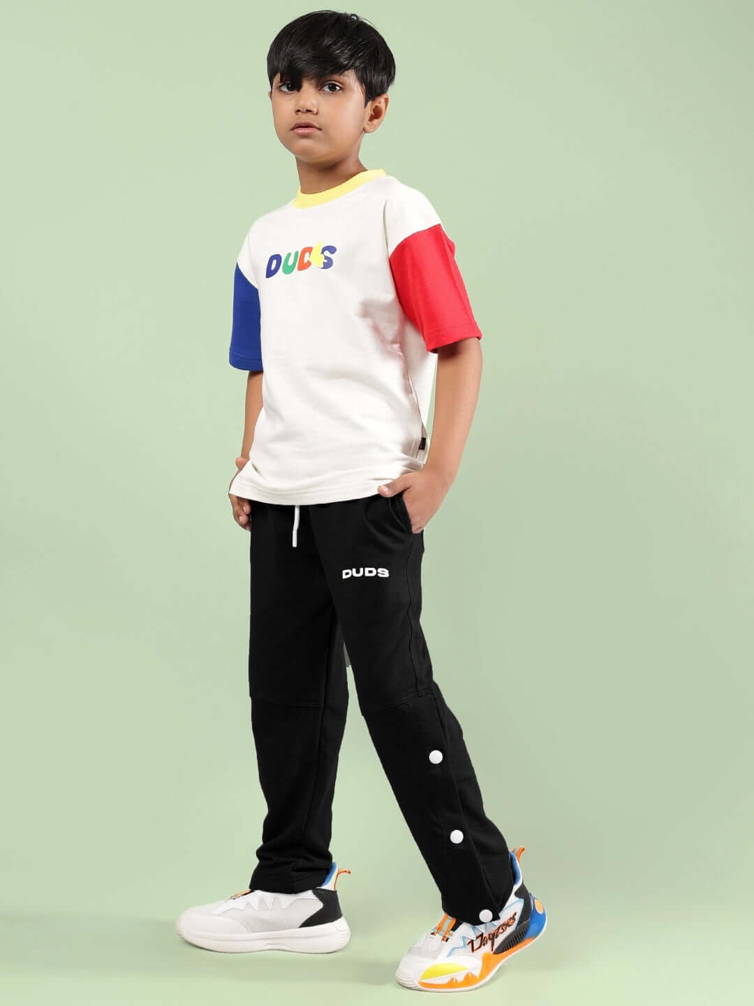 Boy wearing ADONIS CO-ORD FOR BOYS GIRLS OFF WHITE-BLACK, colorful shirt and black pants, standing on a light green background.