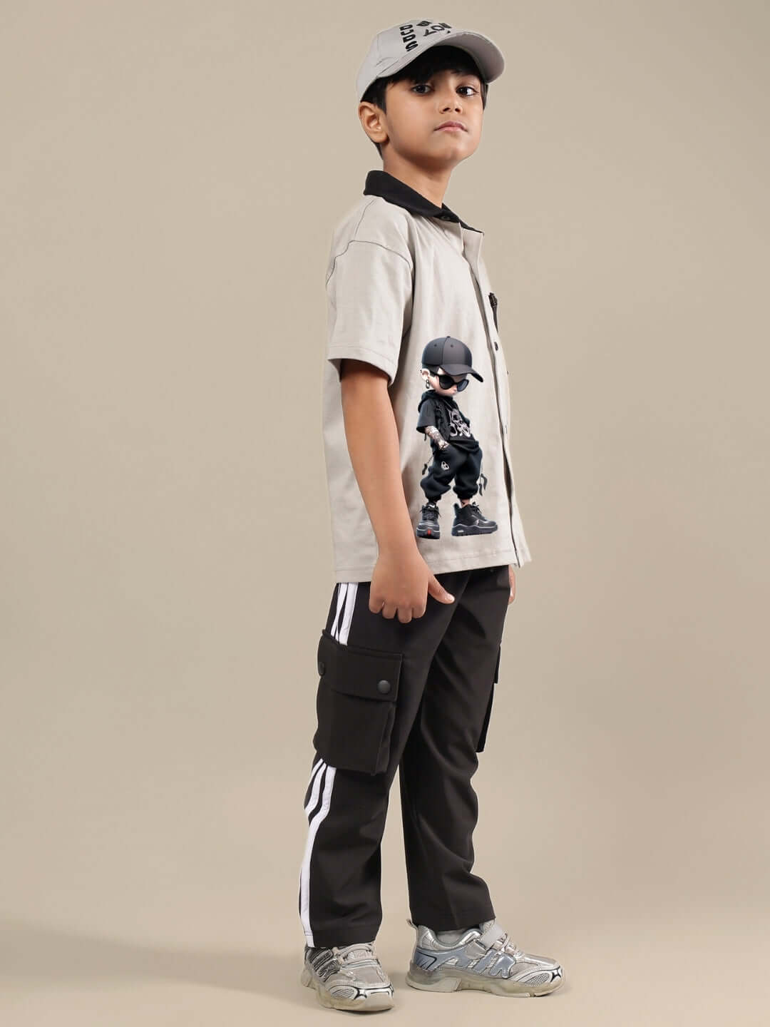 Young boy wearing a grey-black co-ord set, featuring a printed shirt and cargo pants, styled with a cap and sneakers. Ideal for boys & girls.