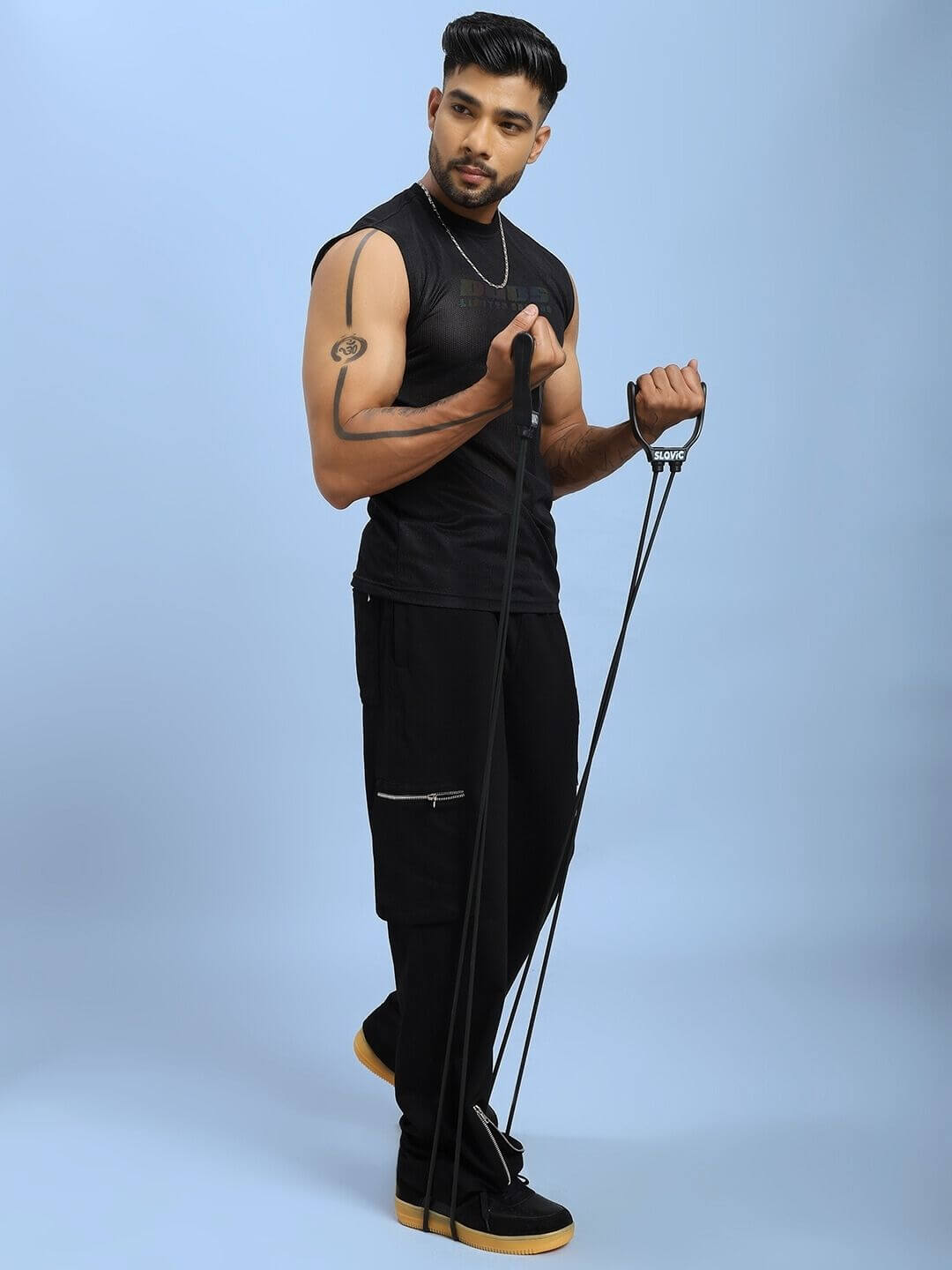Man exercising in AIR-FLOW REGULAR FIT T-SHIRT BLACK with resistance bands on a light blue background.