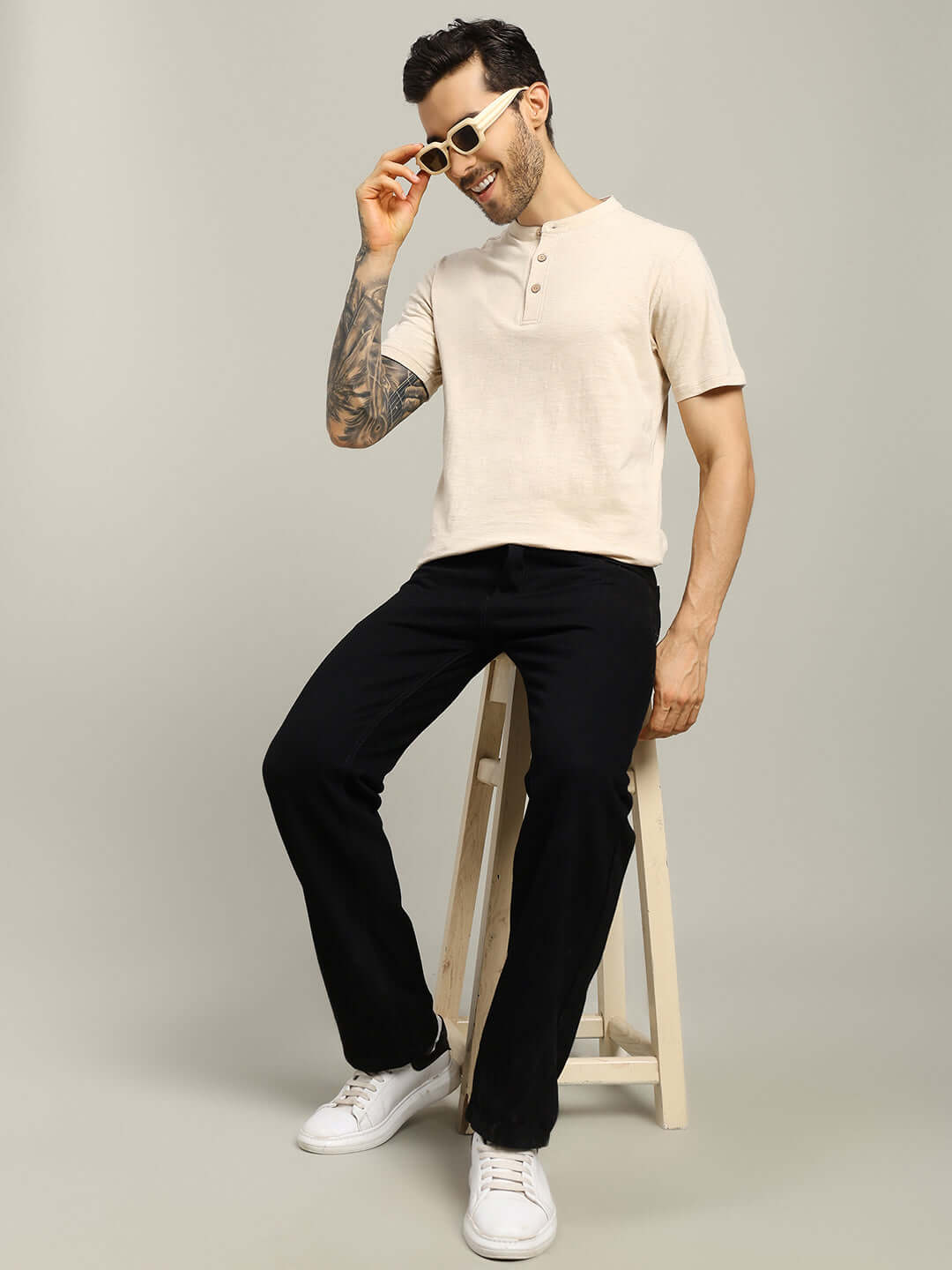 Model wearing ALBET REGULAR FIT T-SHIRT BEIGE paired with black pants sitting on a stool.