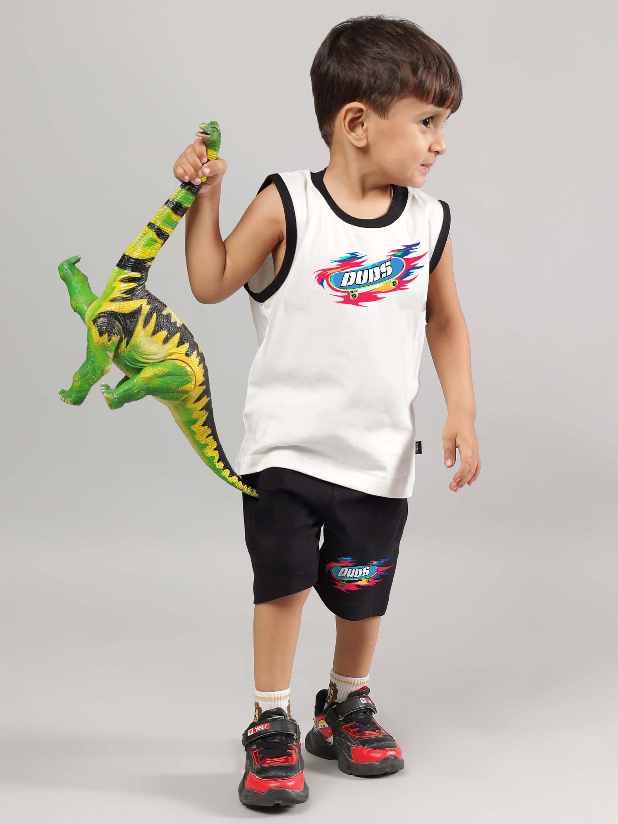 Child wearing black Alien shorts, holding a green toy dinosaur, showcasing DUDS brand casual kidswear.