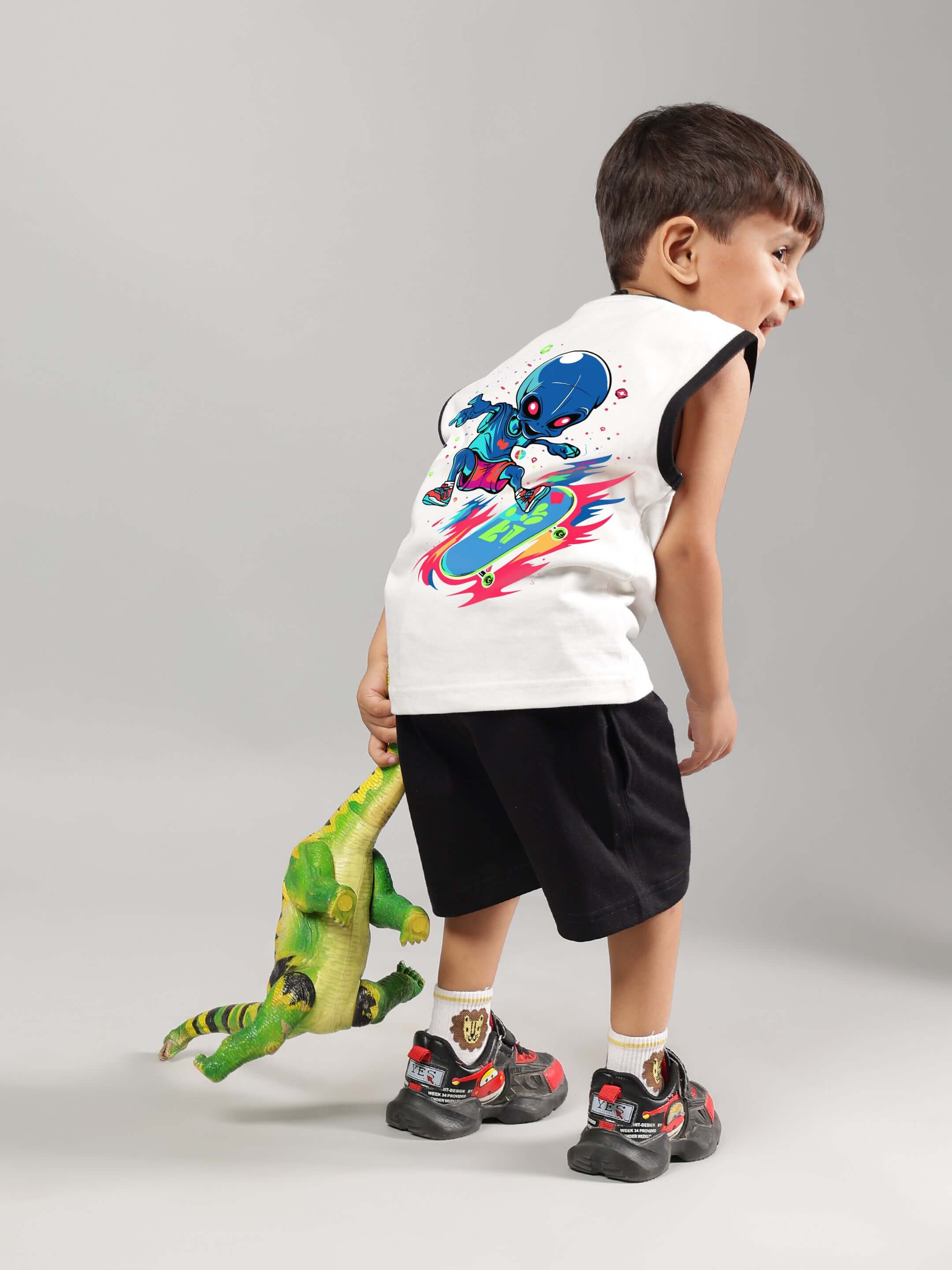 Child wearing ALIEN SUMMER CO-ORD FOR BOYS GIRLS OFF WHITE-BLACK with alien graphic, holding toy dinosaur.