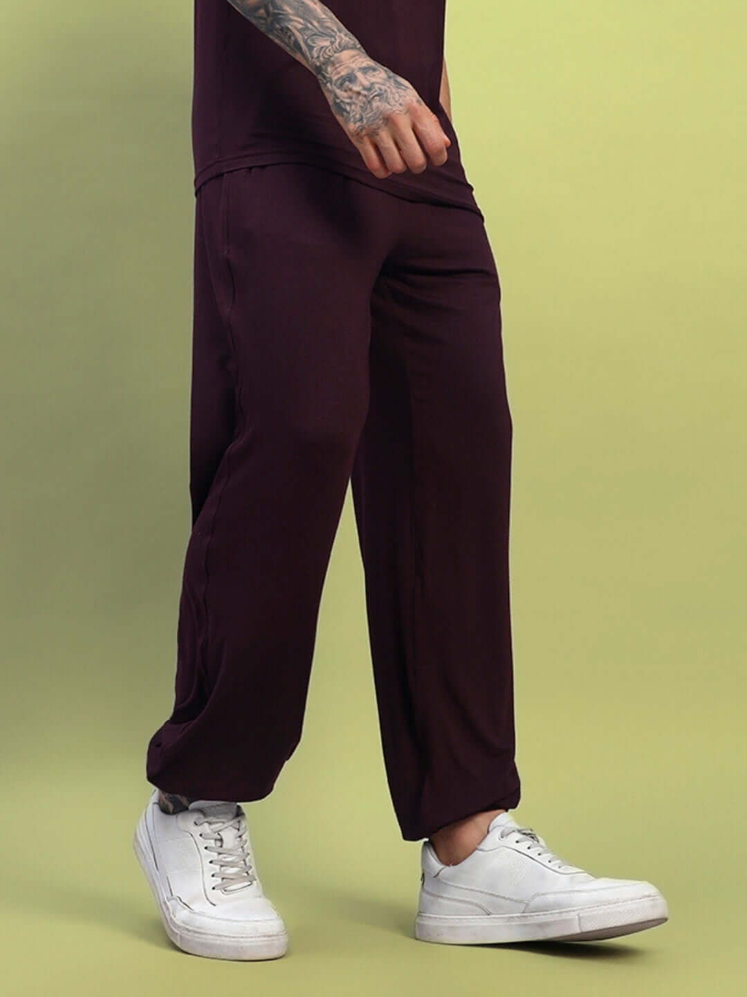 Man wearing Amble Relaxed Fit Jogger Maroon with white sneakers, showcasing a relaxed fit and streetwear style against a yellow background.