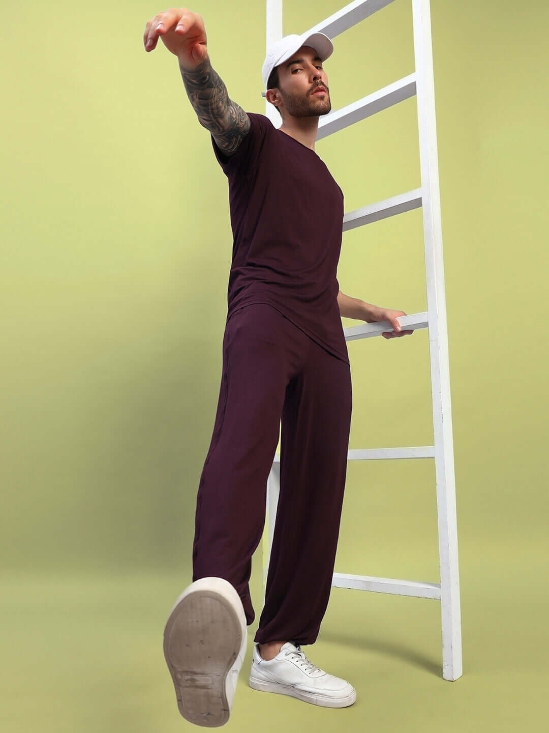 Model wearing maroon AMBLE T-shirt in premium heavy gauge fabric, bio-washed, standing by a ladder with a stylish pose.