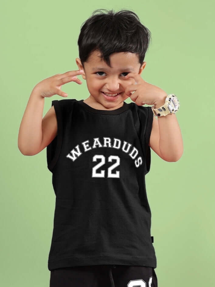 Child wearing AMIGA T-SHIRT FOR BOYS & GIRLS BLACK with 'WEARDUDS 22' print, smiling against green background.