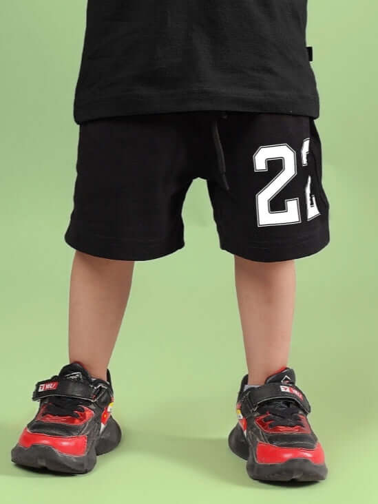 AMIGA SHORTS FOR BOYS & GIRLS BLACK WHITE worn by child with red and black sneakers on green background