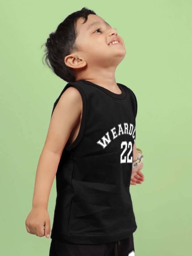 Child wearing AMIGA T-SHIRT FOR BOYS & GIRLS BLACK, with a playful pose on a green background. Unisex design with white lettering.