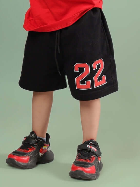 Child wearing AMIGA SHORTS FOR BOYS & GIRLS BLACK RED with number 22 and red sneakers.
