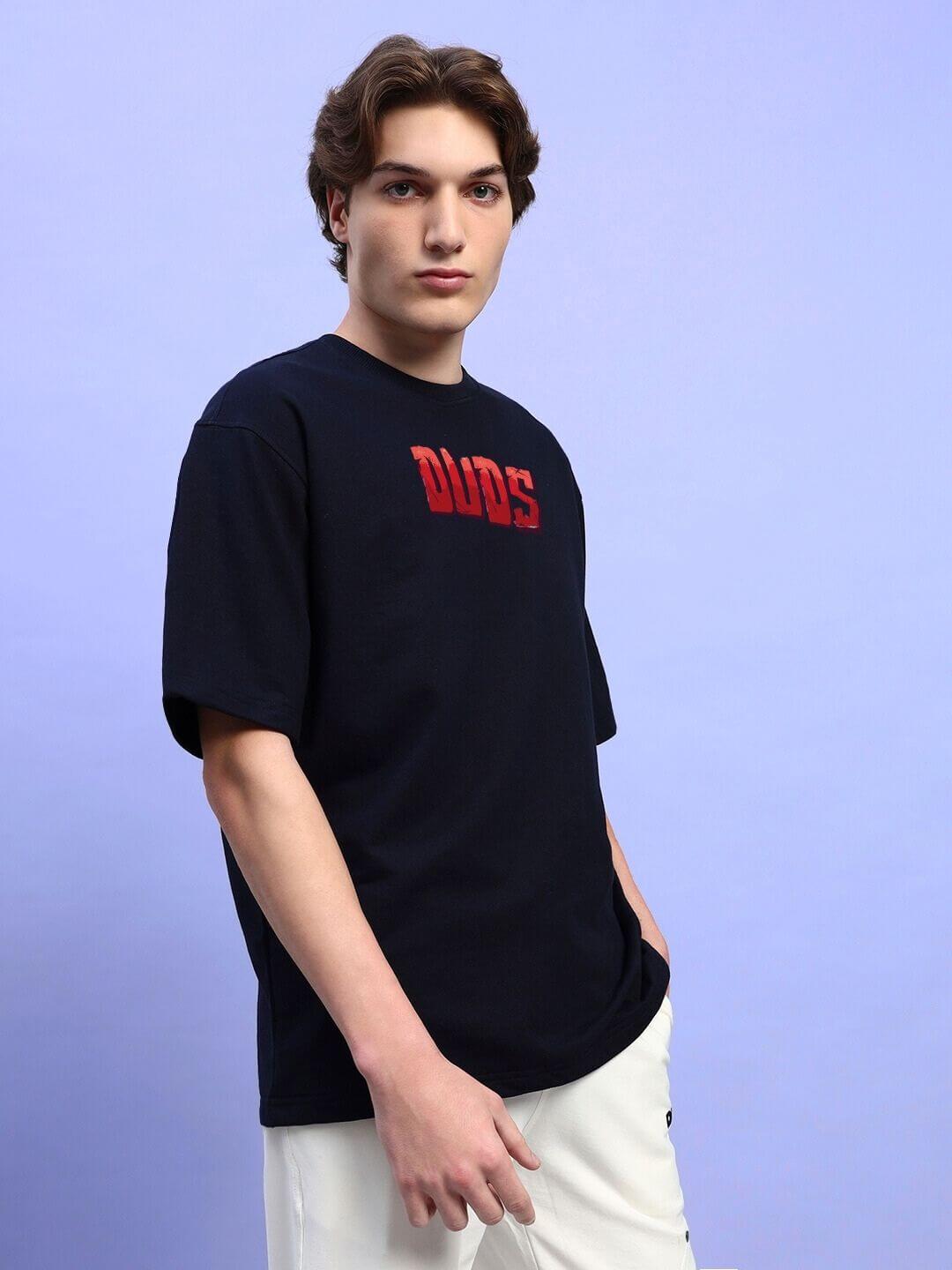 Model wearing AMPERES PRINT OVERSIZED T-SHIRT BLACK with urban design, showcasing streetwear style on light background.