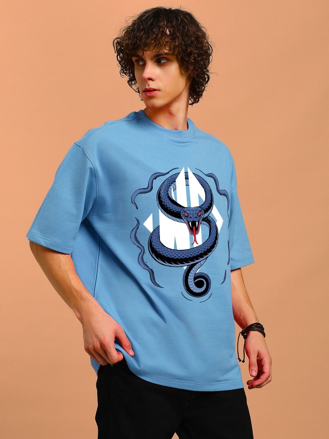 Man wearing ANGRY SNAKE WD PRINTED OVERSIZED T-SHIRT LIGHT BLUE standing against a brown background with curly hair.