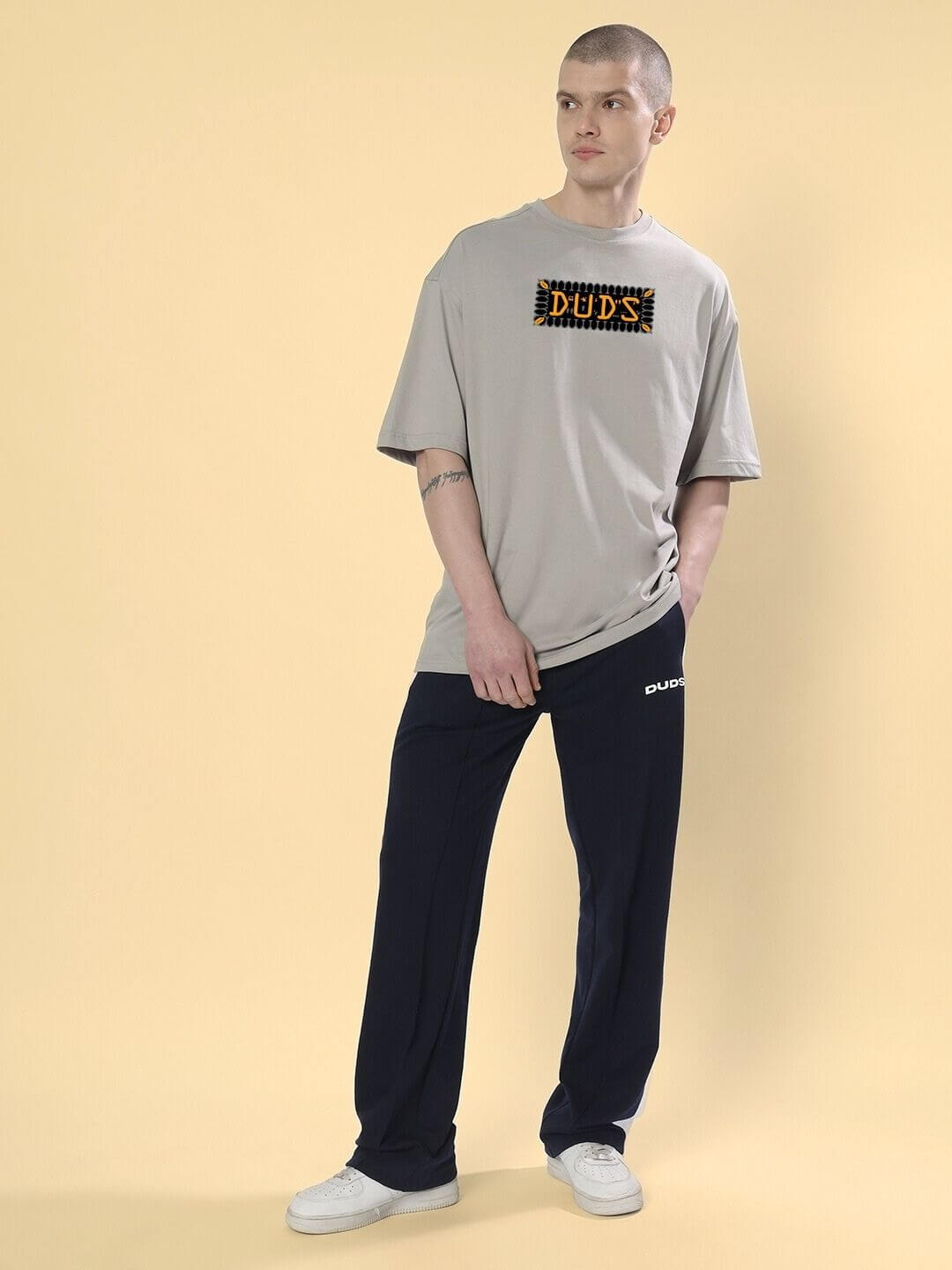 Man wearing ANUBIS EGYPTIAN PRINTED OVERSIZED T-SHIRT GREY with black pants standing against a yellow background.