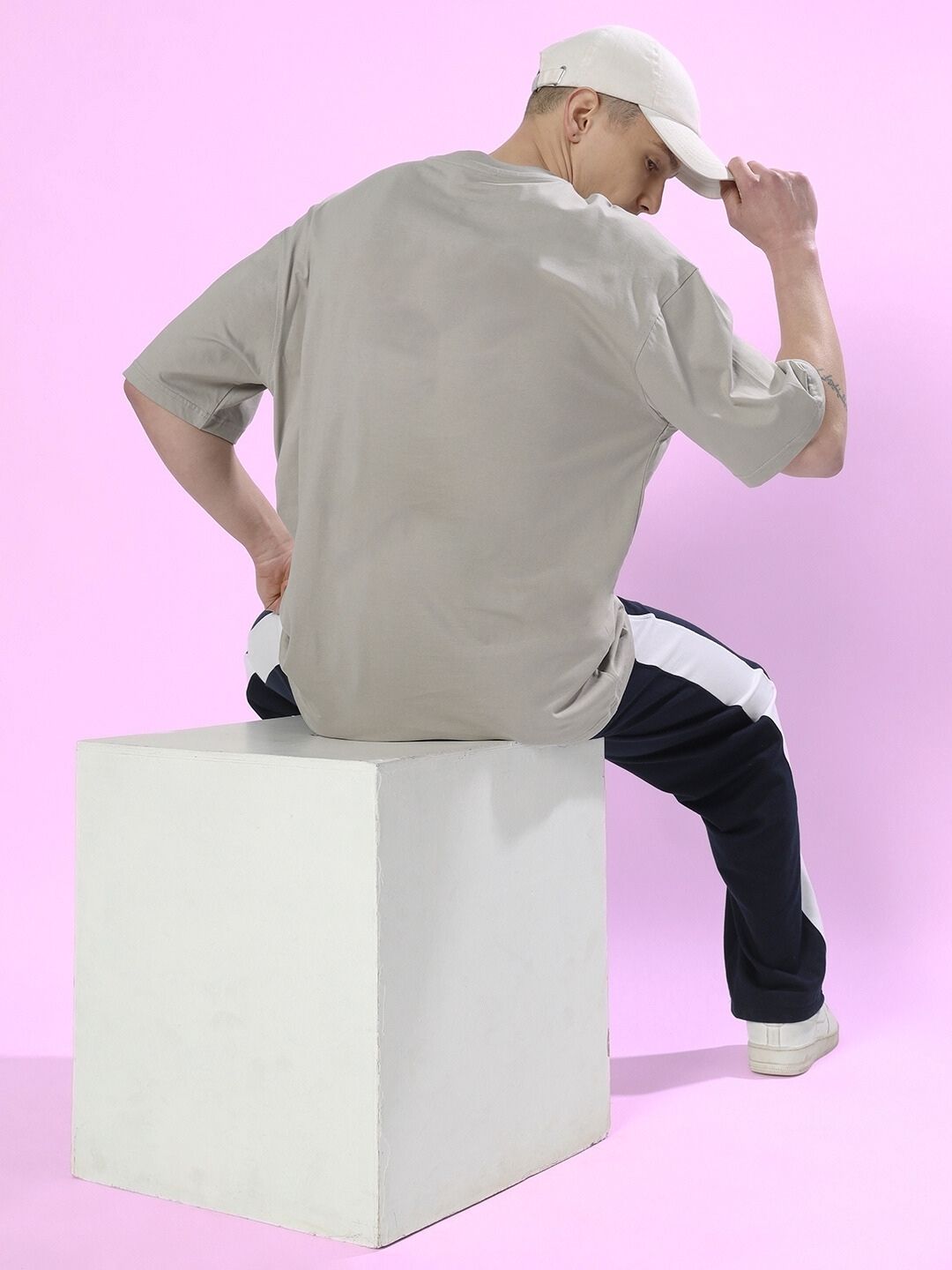 Model wearing ANXIETY OVER-SIZED T-SHIRT GREY sitting on a white cube against a pink background
