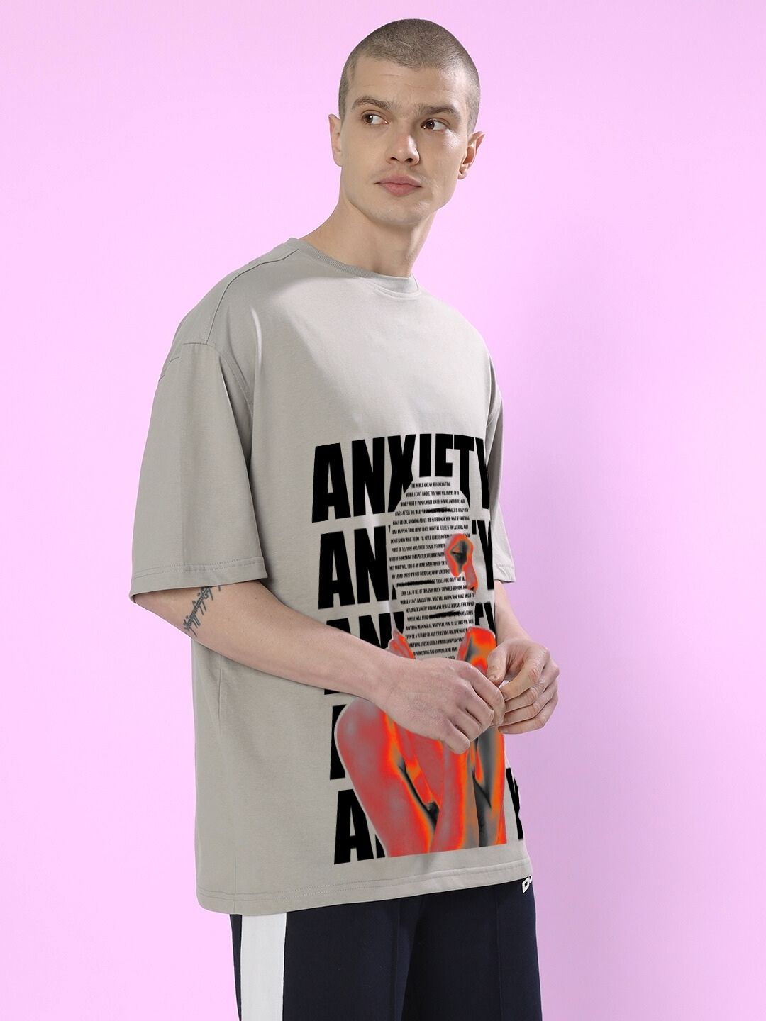 Model wearing ANXIETY OVER-SIZED T-SHIRT GREY with bold graphic design against a pink background.