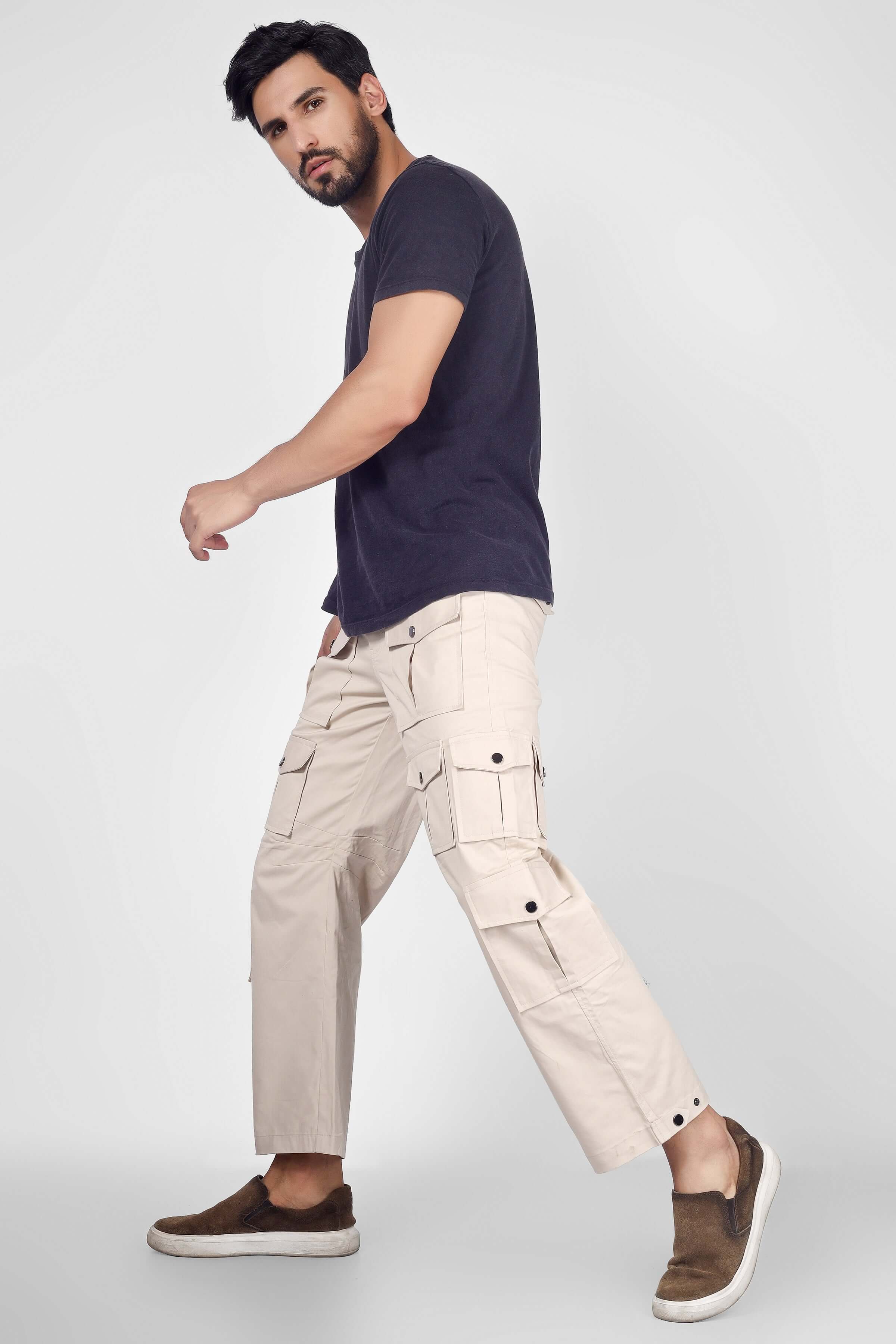 Man wearing Arcadia White 14 Pocket Cargo Pants, beige color, with black t-shirt, showcasing modern, stylish design and comfortable fit.