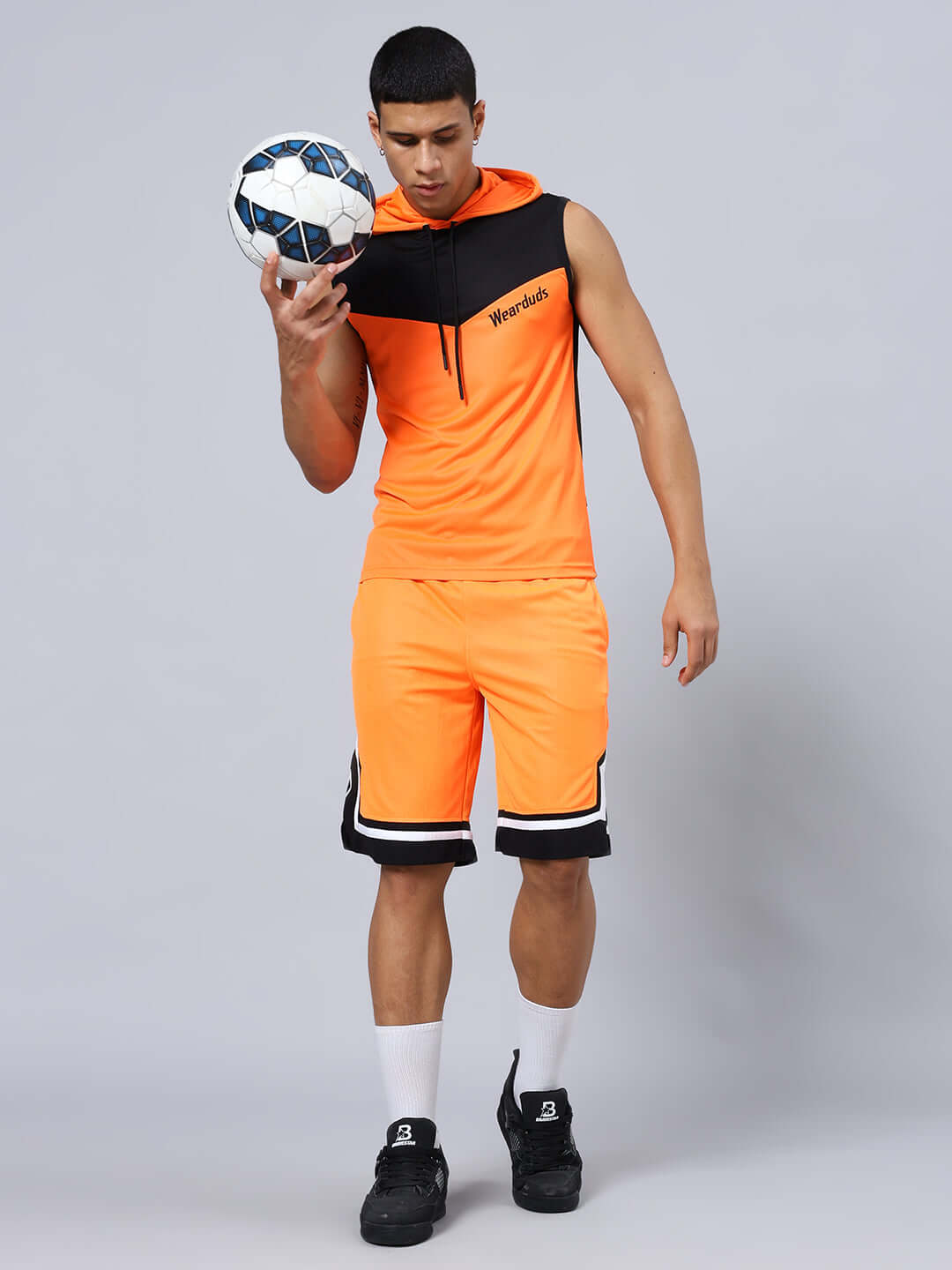 ARMADO REGULAR FIT SHORTS ORANGE BLACK Man wearing Armado regular fit orange black shorts with matching top, holding a soccer ball, showcasing sporty style and casual attire.