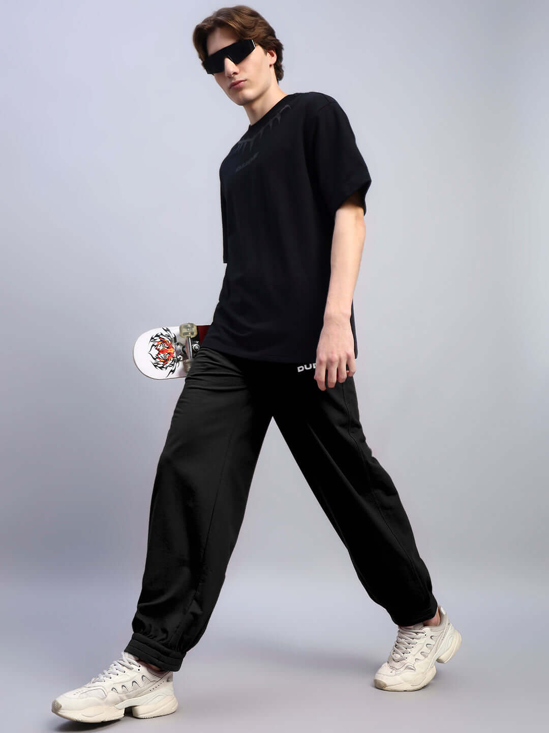 Model wearing AUSTRIAN RELAXED-FIT JOGGERS BLACK paired with sneakers and black top, showcasing sleek streetwear style.
