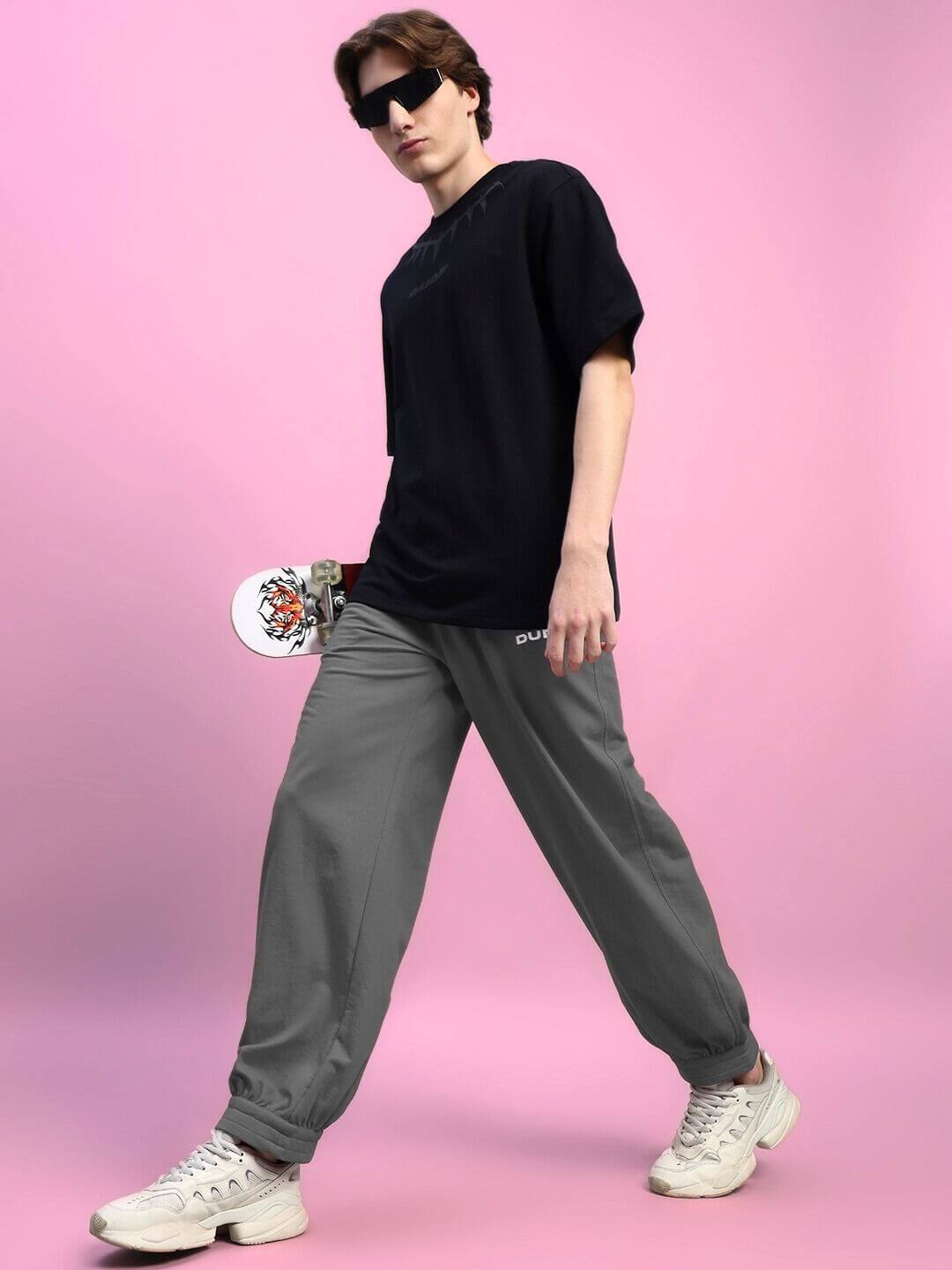 Man wearing Austrian Relaxed-Fit Joggers Grey, holding skateboard; showcases modern streetwear style.