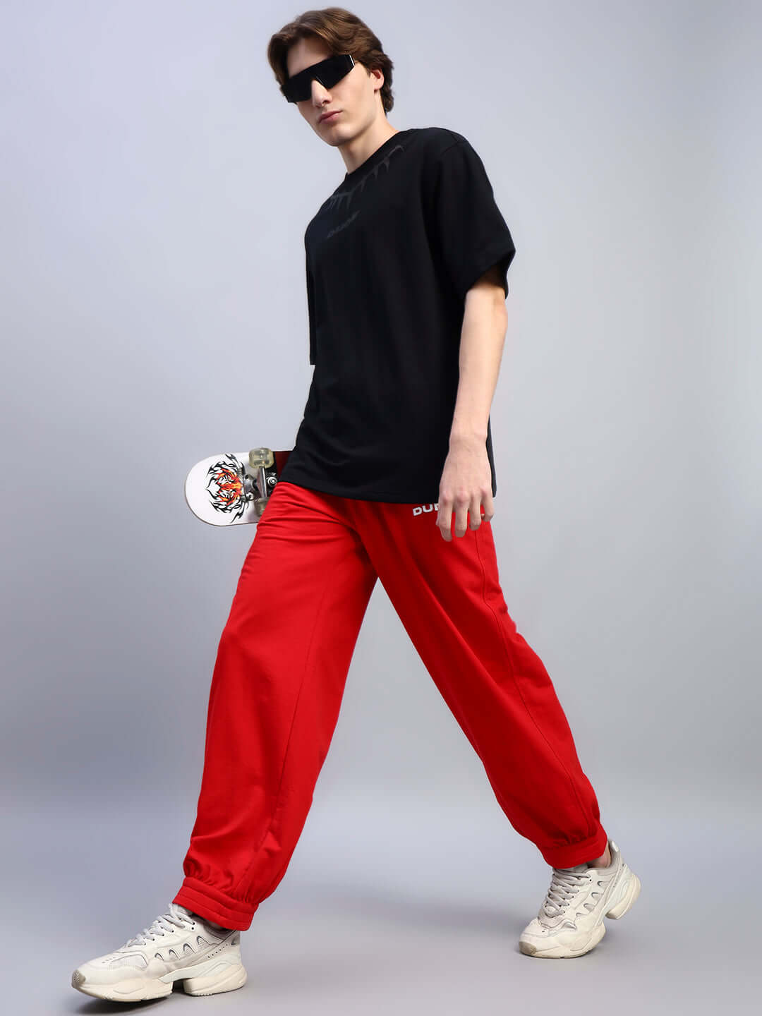 Person wearing AUSTRIAN RELAXED-FIT JOGGERS RED and black shirt with skateboard in hand, showcasing casual streetwear style.