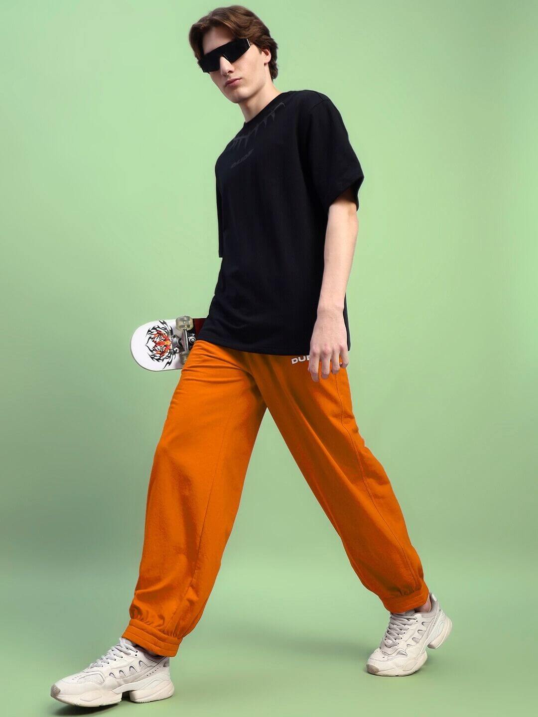 Fashionable person wearing AUSTRIAN RELAXED-FIT JOGGERS ORANGE, showcasing athleisure style with skateboard.