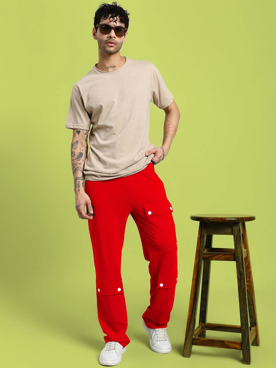 Person wearing AWESOME FLAP POCKET BAGGY JOGGER RED, standing next to a stool, showcasing bold streetwear style.