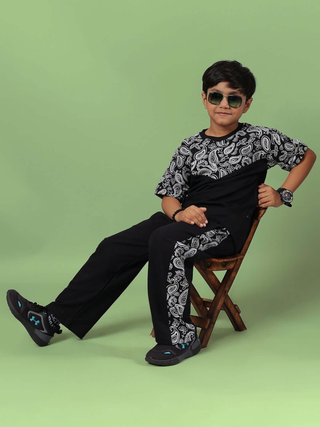 Young boy wearing BalaDeer Co-Ord for Boys & Girls Black, sitting confidently in stylish sporty outfit on a chair, showcasing trendy fashion.