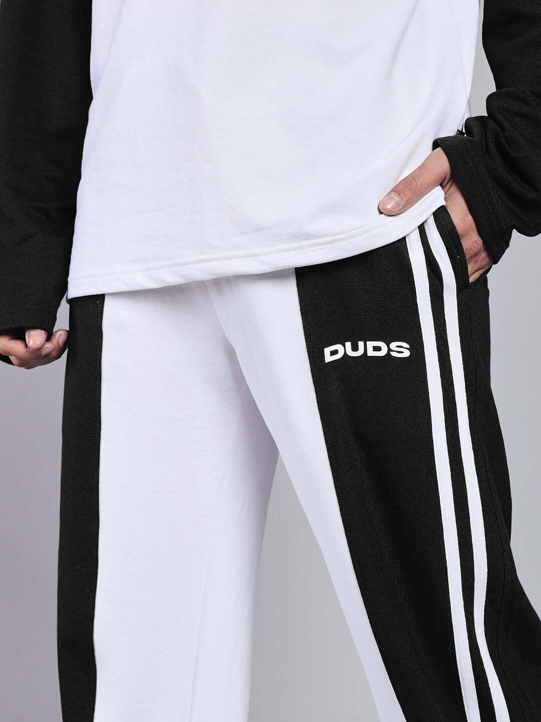 Person wearing white-black relaxed fit joggers with 'DUDS' logo, highlighting stylish design and comfort.