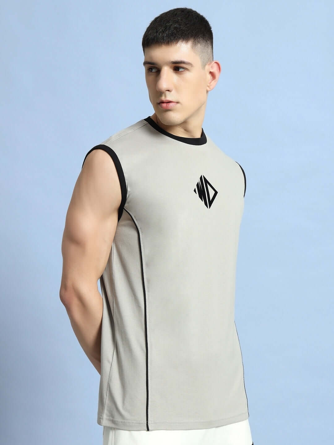 Alt Tag: Male model wearing BARE ARMS GYM T-SHIRT in grey with logo, showcasing sleeveless design against a blue background.
