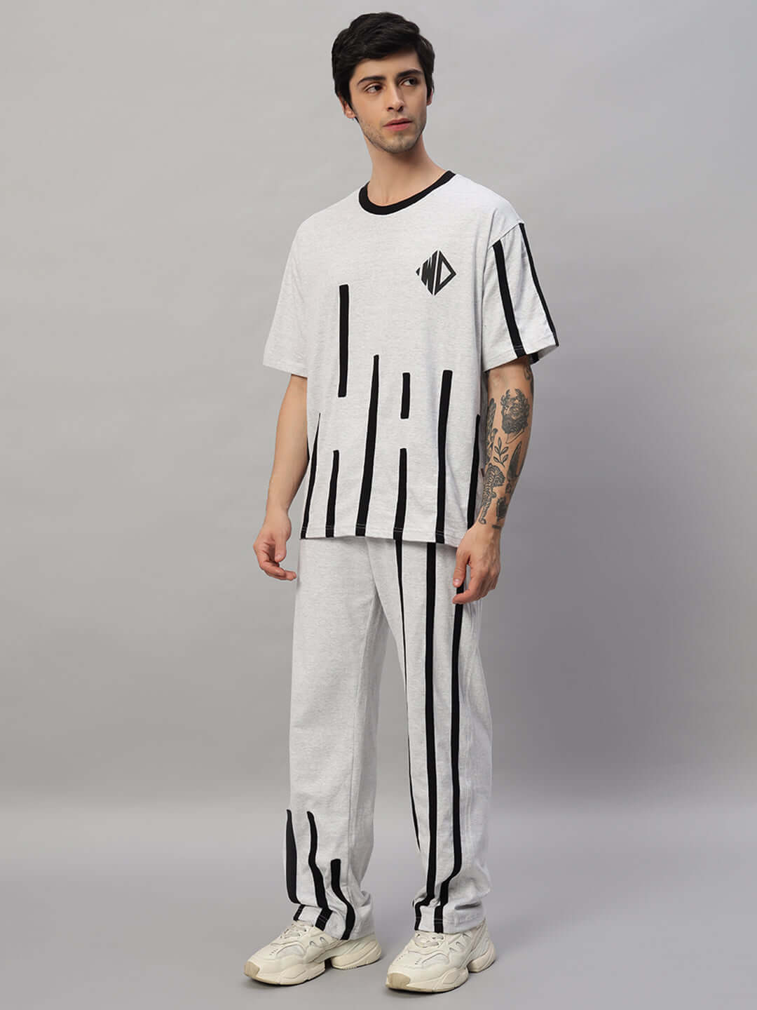 Model wearing BASTILLE OVERSIZED CO-ORD SET MELANGE GREY with vertical stripes and sneakers, showcasing relaxed fit and modern style.