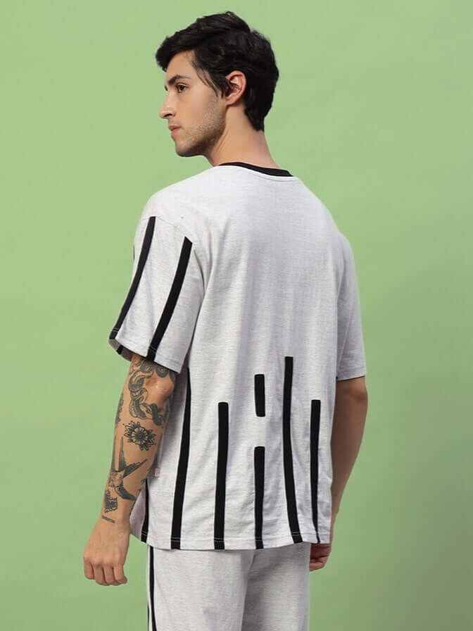 Man wearing BASTILLE OVERSIZED T-SHIRT MELANGE GREY with black stripes on a green background, showcasing back design