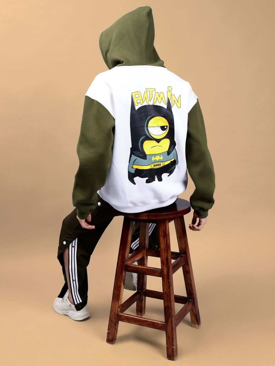 Back view of Batmin Colorblock Oversized Fleece Hoodie in white and olive green with graphic design, seated on a stool.